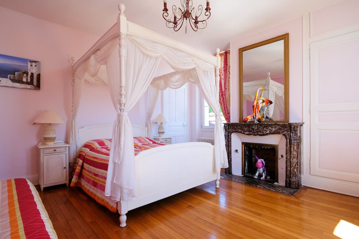 A bedroom with a four-poster bed, a fireplace, a mirror, and a view of the outside.