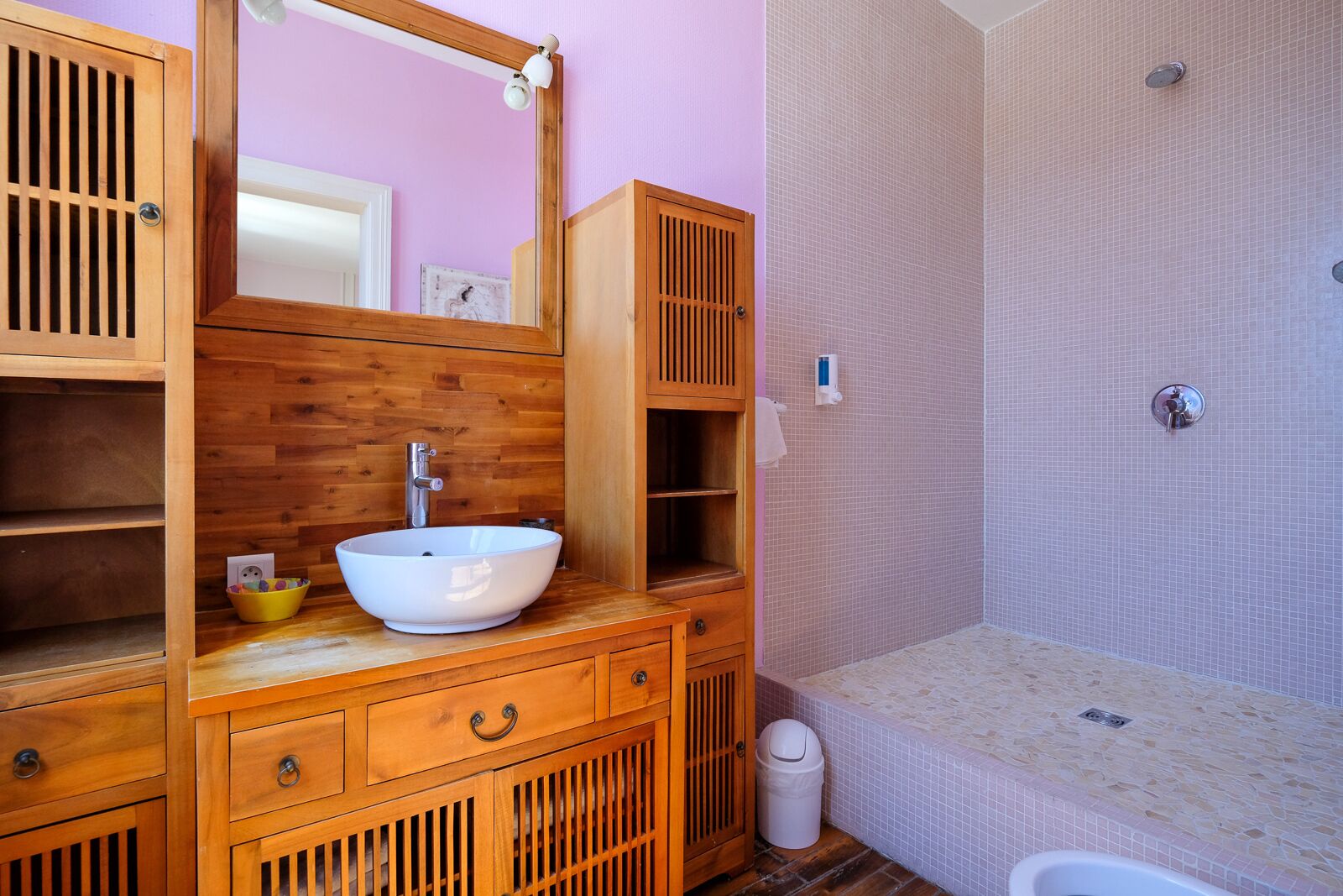 A bathroom with a wooden vanity, a white sink, and a shower area.