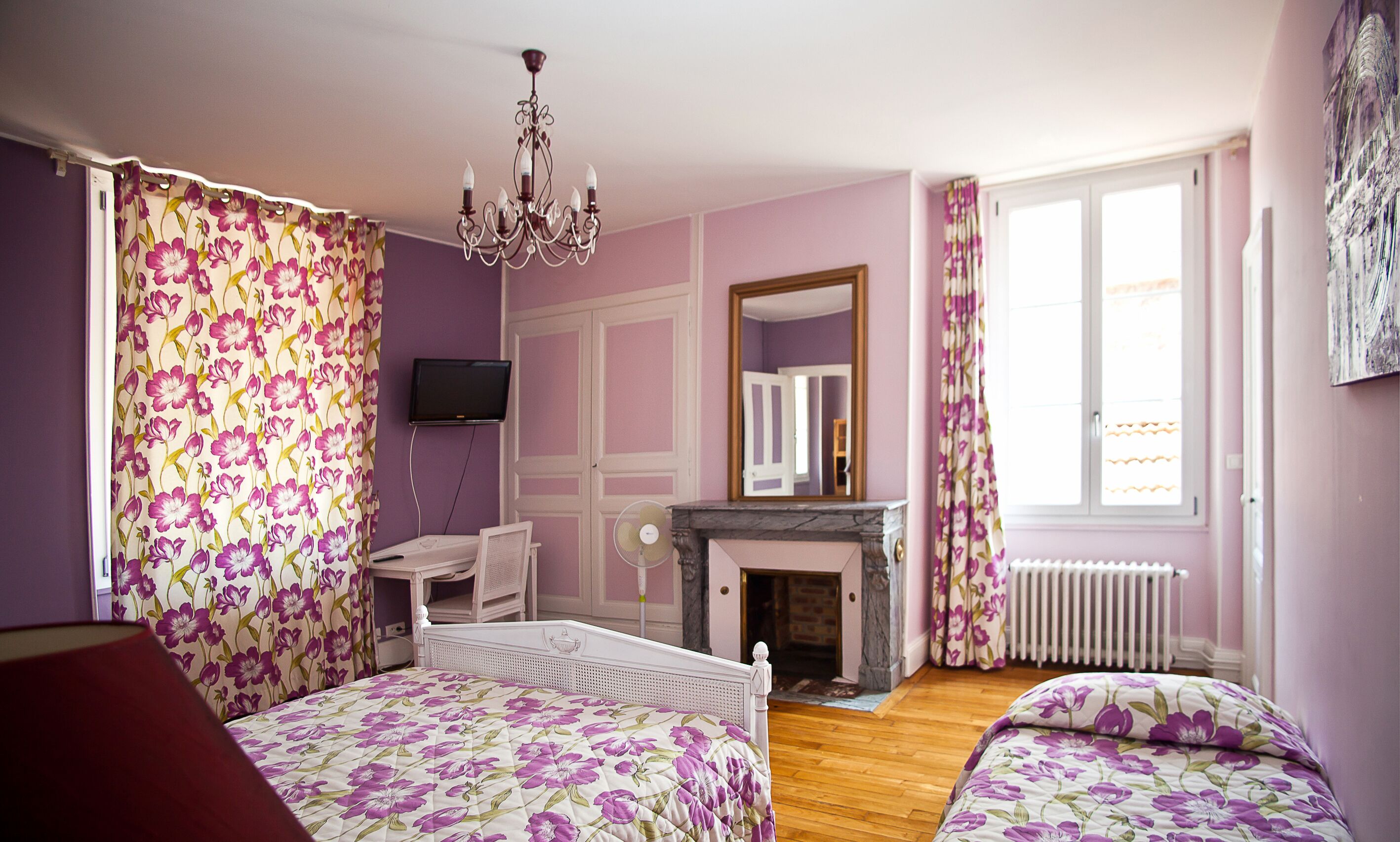 A bedroom with a bed, a chair, a television, a fireplace, and a window.