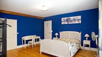 A bedroom with a white bed, a desk, a chair, a nightstand, and a wall-mounted lamp.