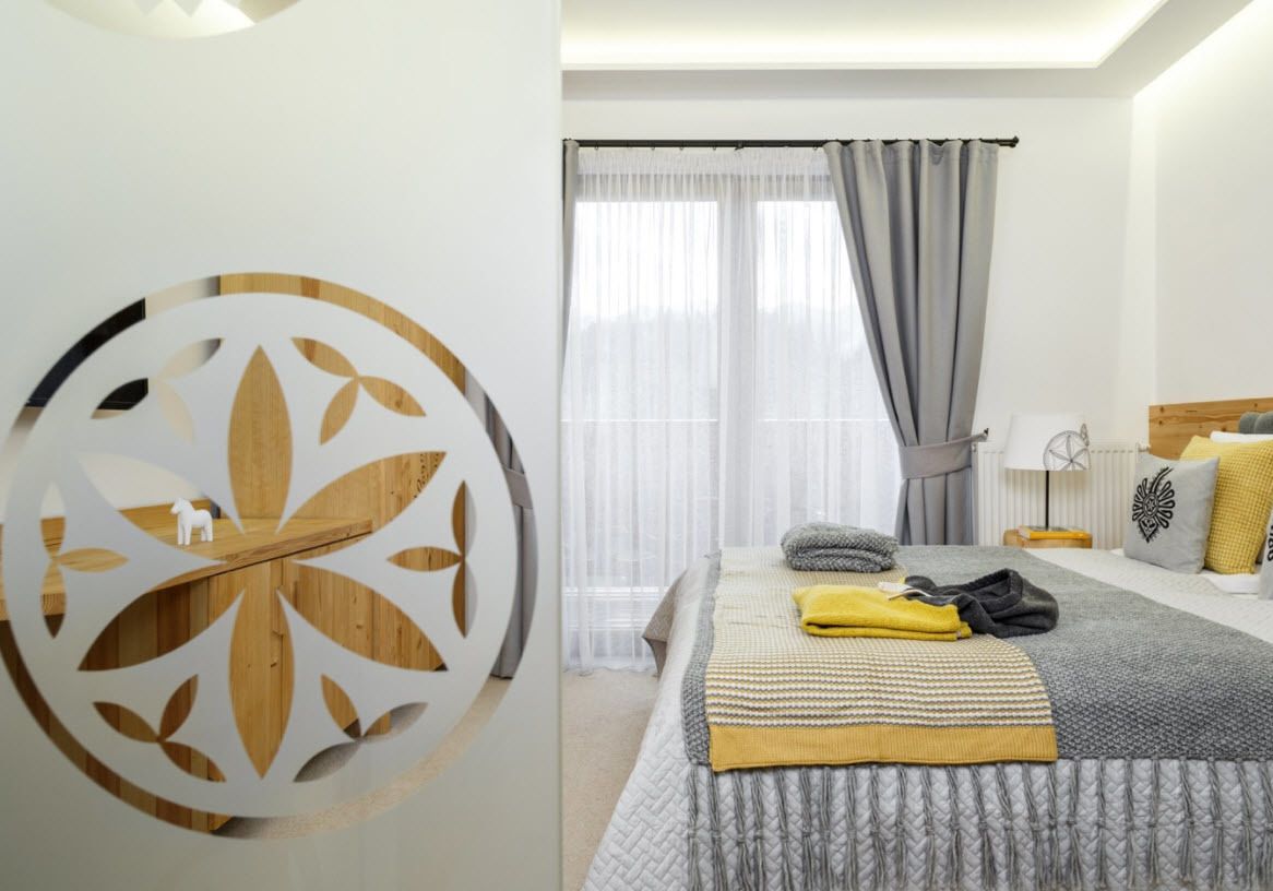 A modern hotel room with a large bed, a decorative wall piece, and a view of the outdoors through sheer curtains.