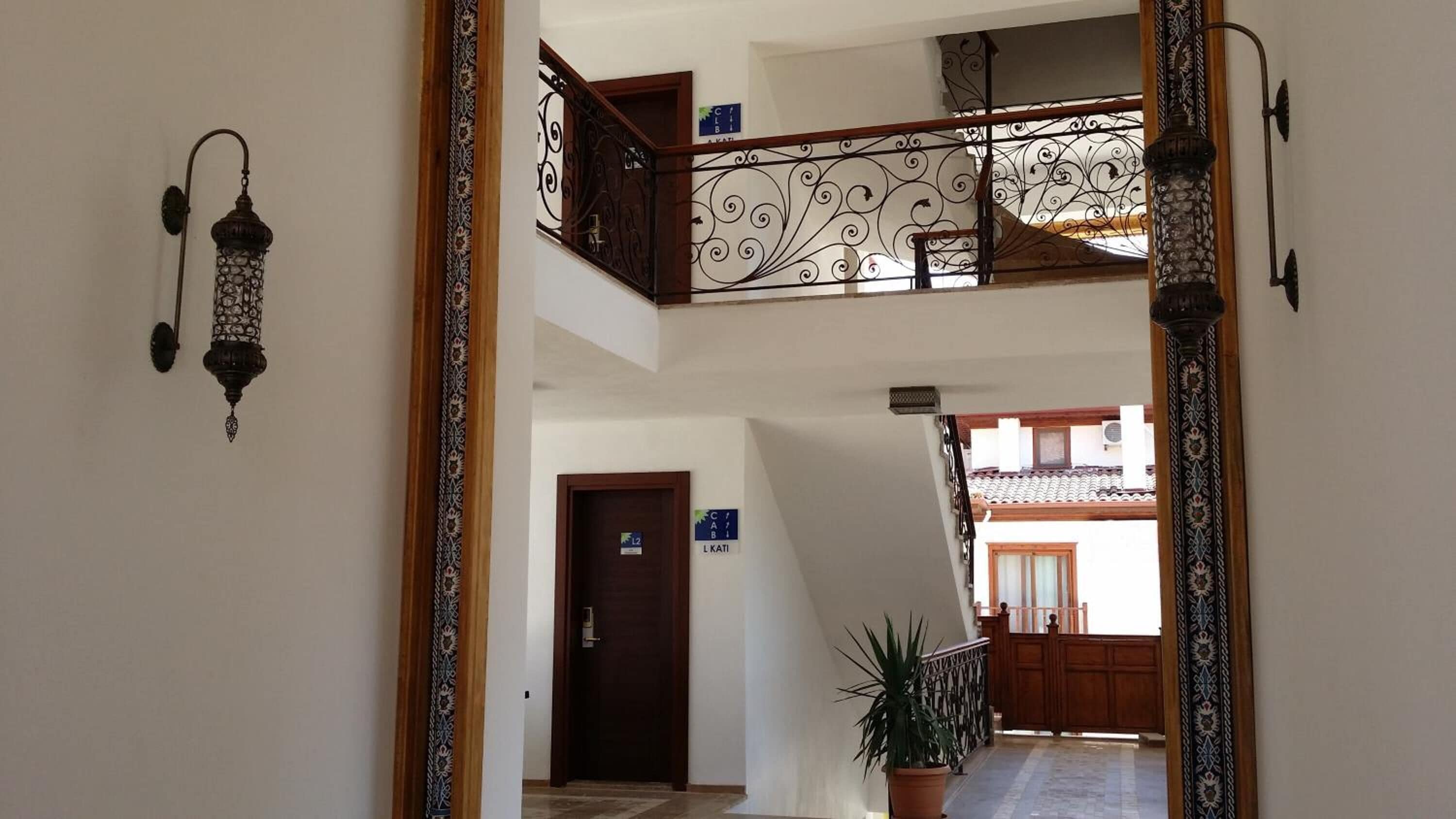 Un corridoio con una porta in legno, una pianta in vaso e una scala con ringhiere in metallo finemente decorate.