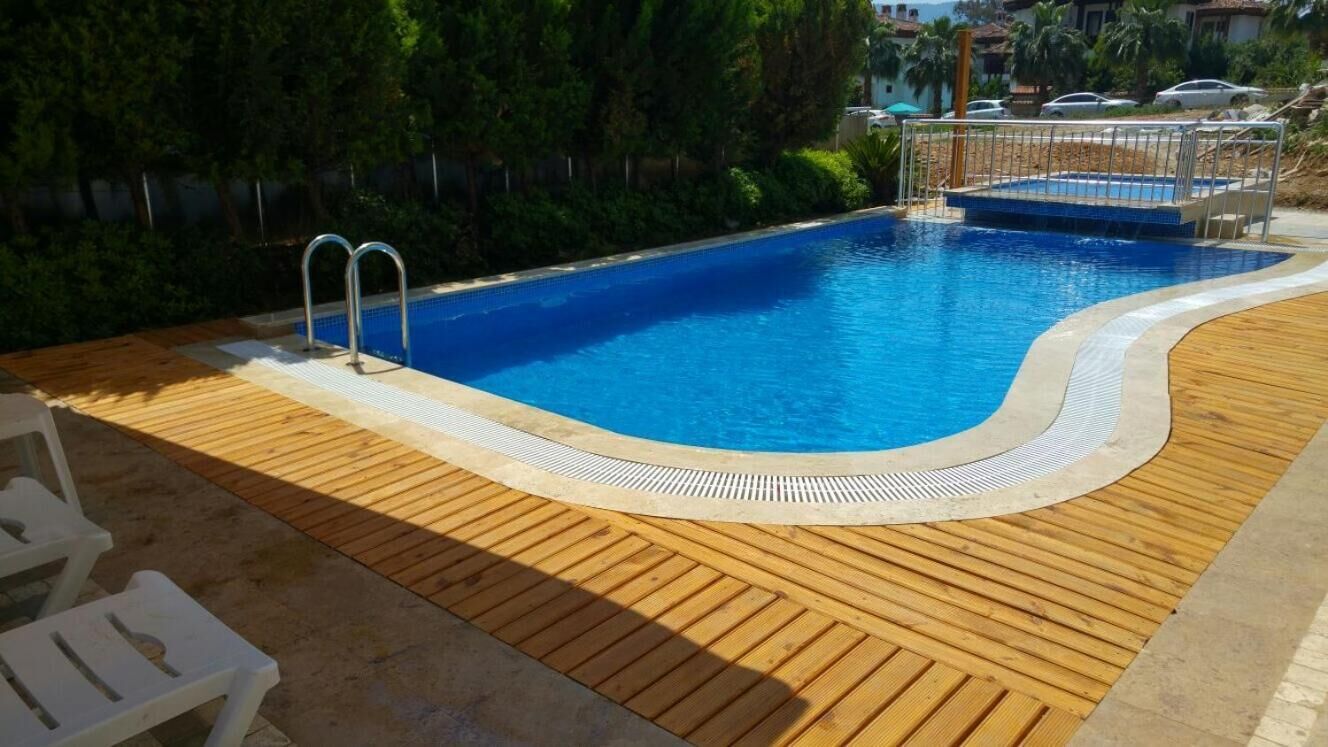 A swimming pool with a wooden deck, metal ladder, and a poolside area with chairs.