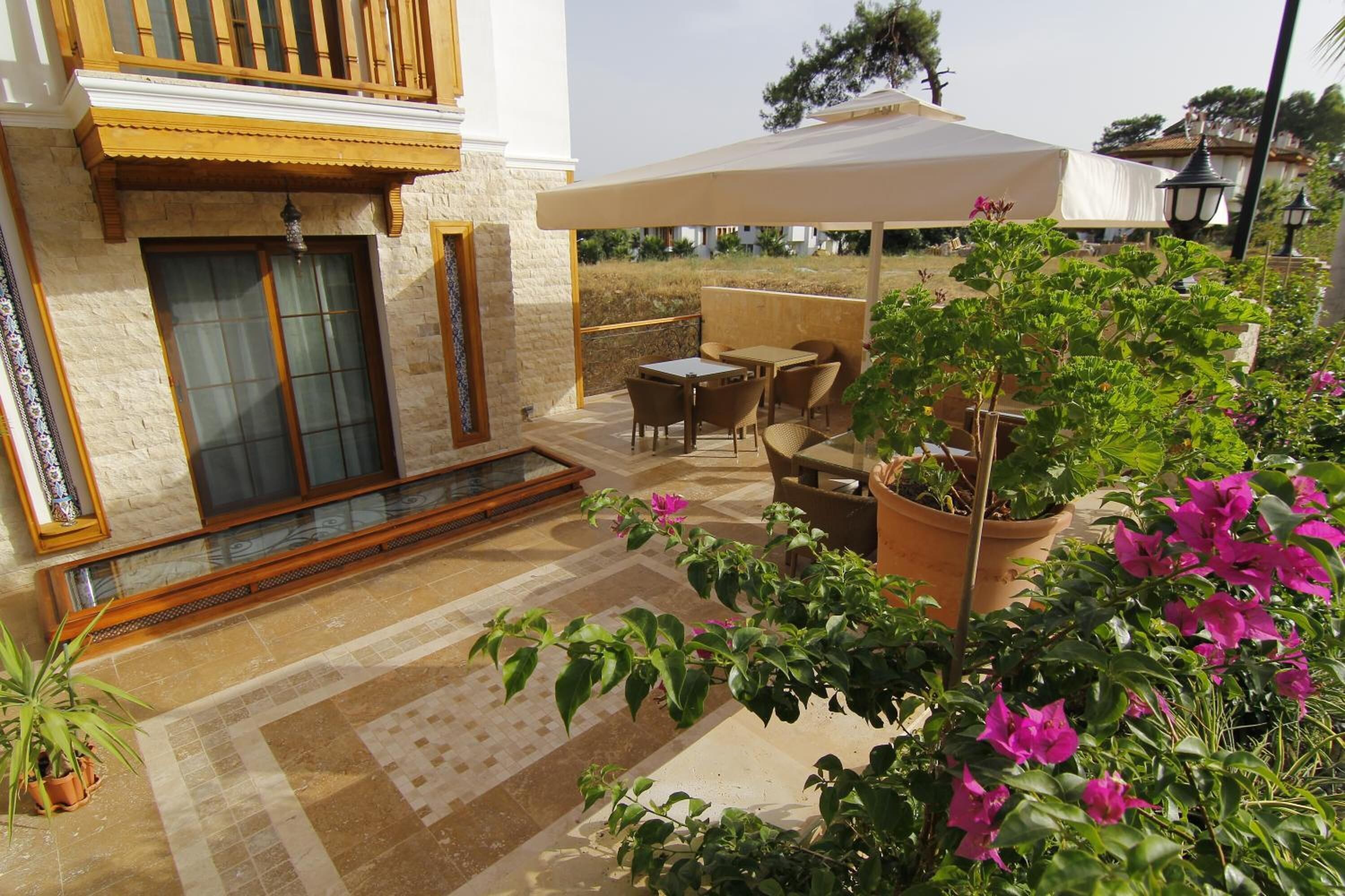 A covered outdoor seating area with tables and chairs, surrounded by potted plants and flowers.