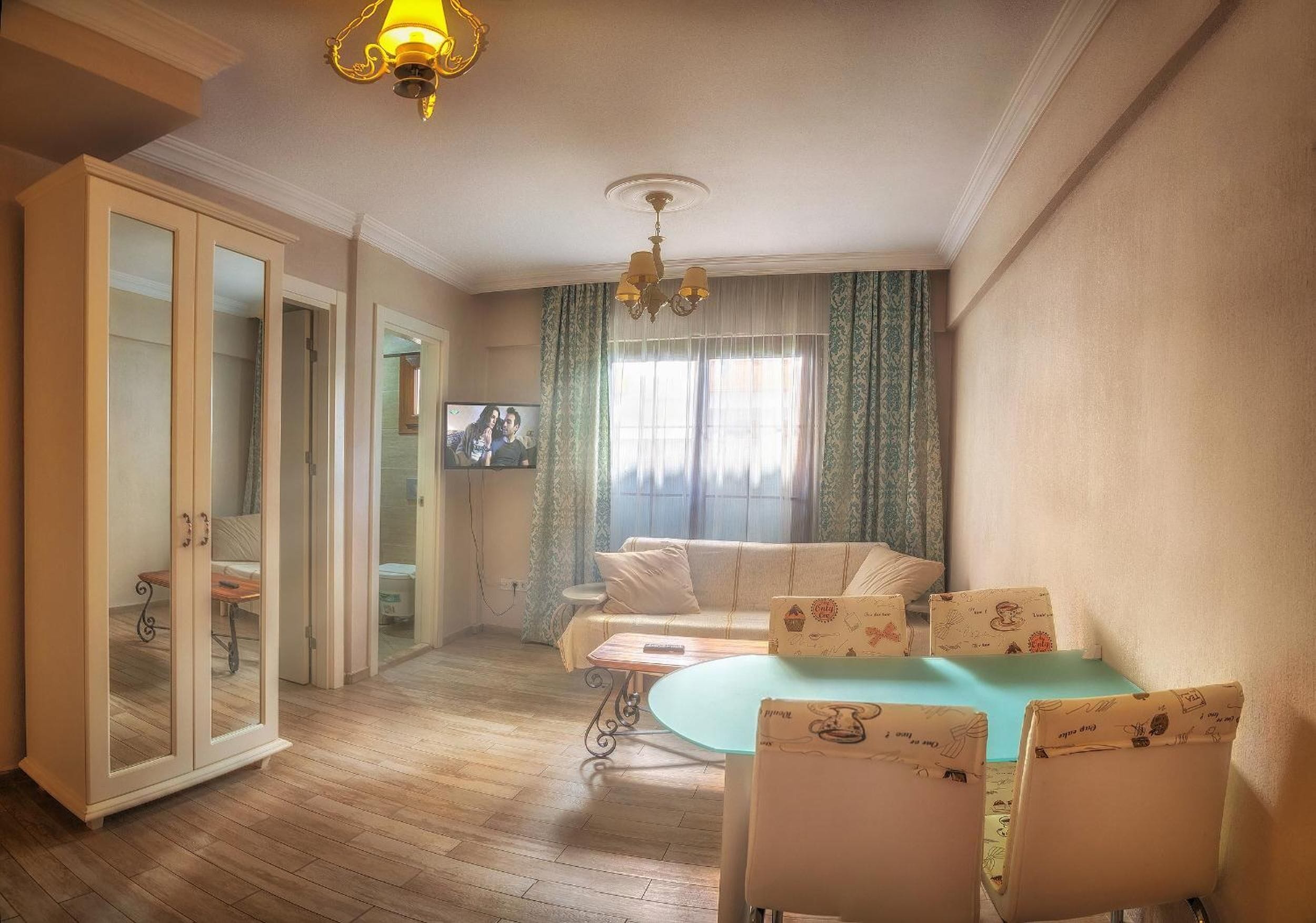 Una sala de estar con un sofá, una mesa y un televisor. Hay un aparador con puertas de vidrio y una araña.