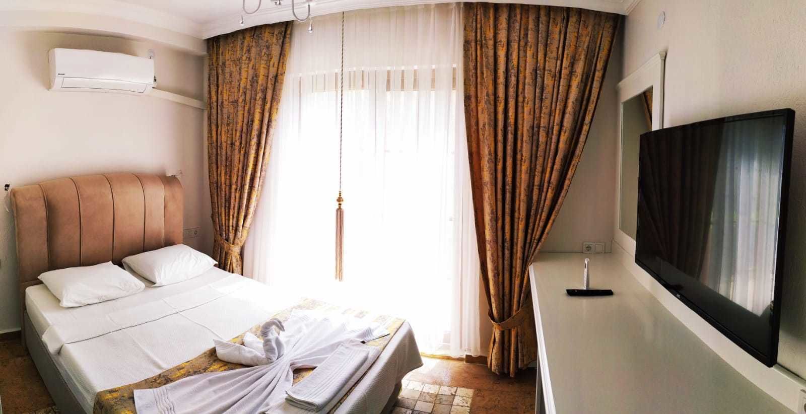 A hotel room with a bed, a flat-screen TV, and a large window with curtains.