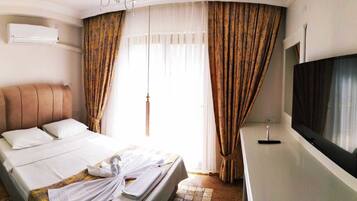 A hotel room with a bed, a flat-screen TV, and a large window with curtains.