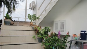 A staircase with potted plants, a white wall with a window, and a metal shelf with various items.