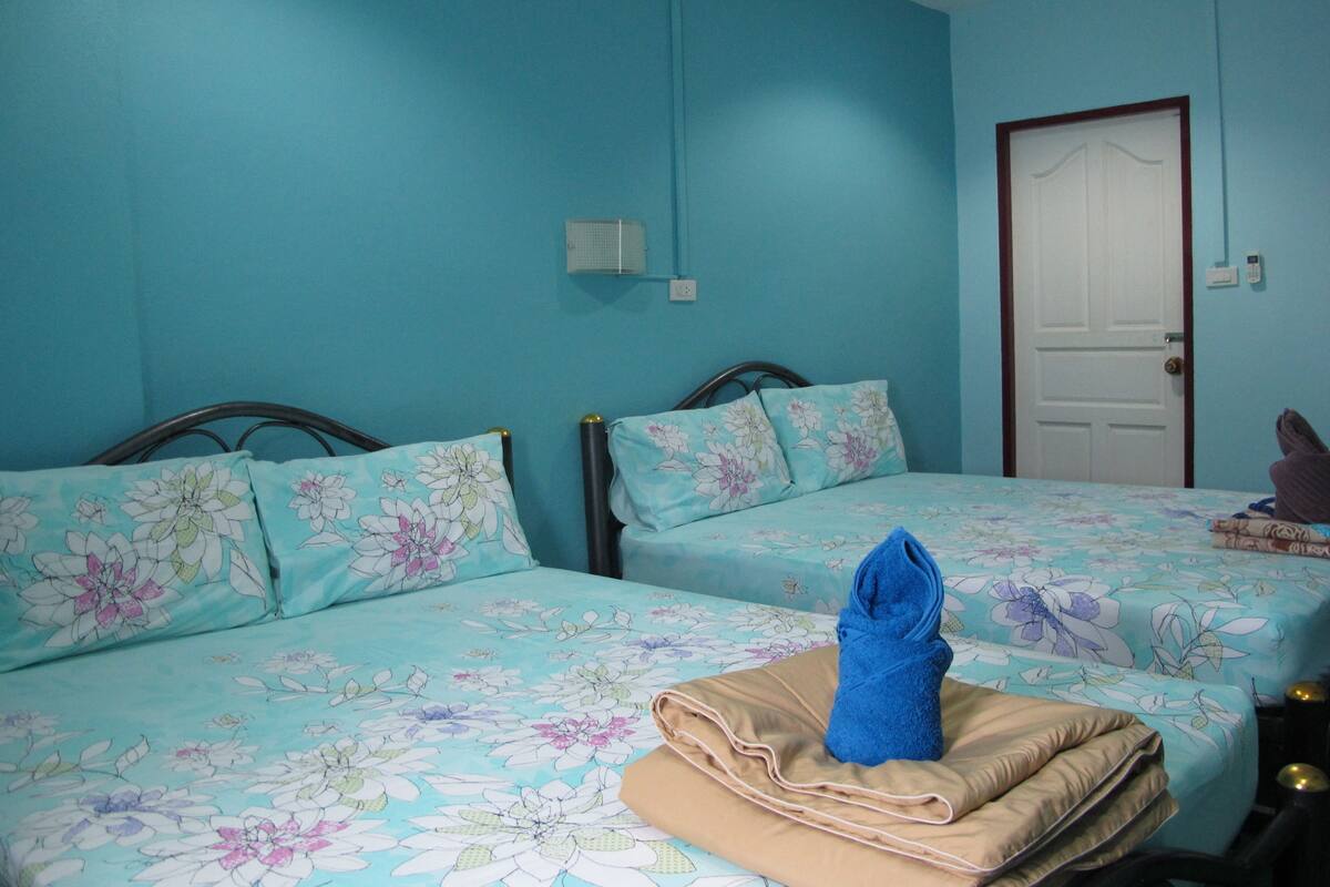 Une chambre avec deux lits, chacun agrémenté de draps à motifs floraux, un mur bleu et une porte.