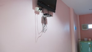 A pink-walled room with a mounted television, a wall-mounted air conditioner, and a green refrigerator.