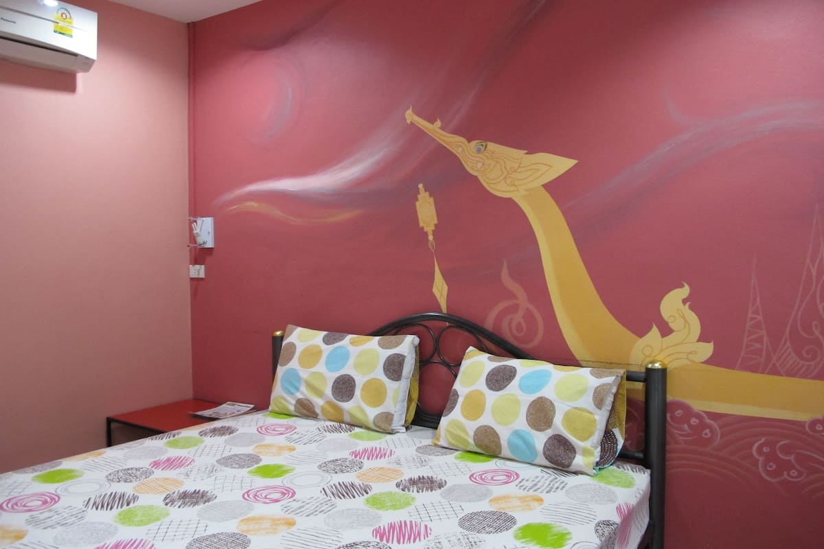 Une chambre à coucher avec un lit, des oreillers, un mur rouge et une fresque murale.