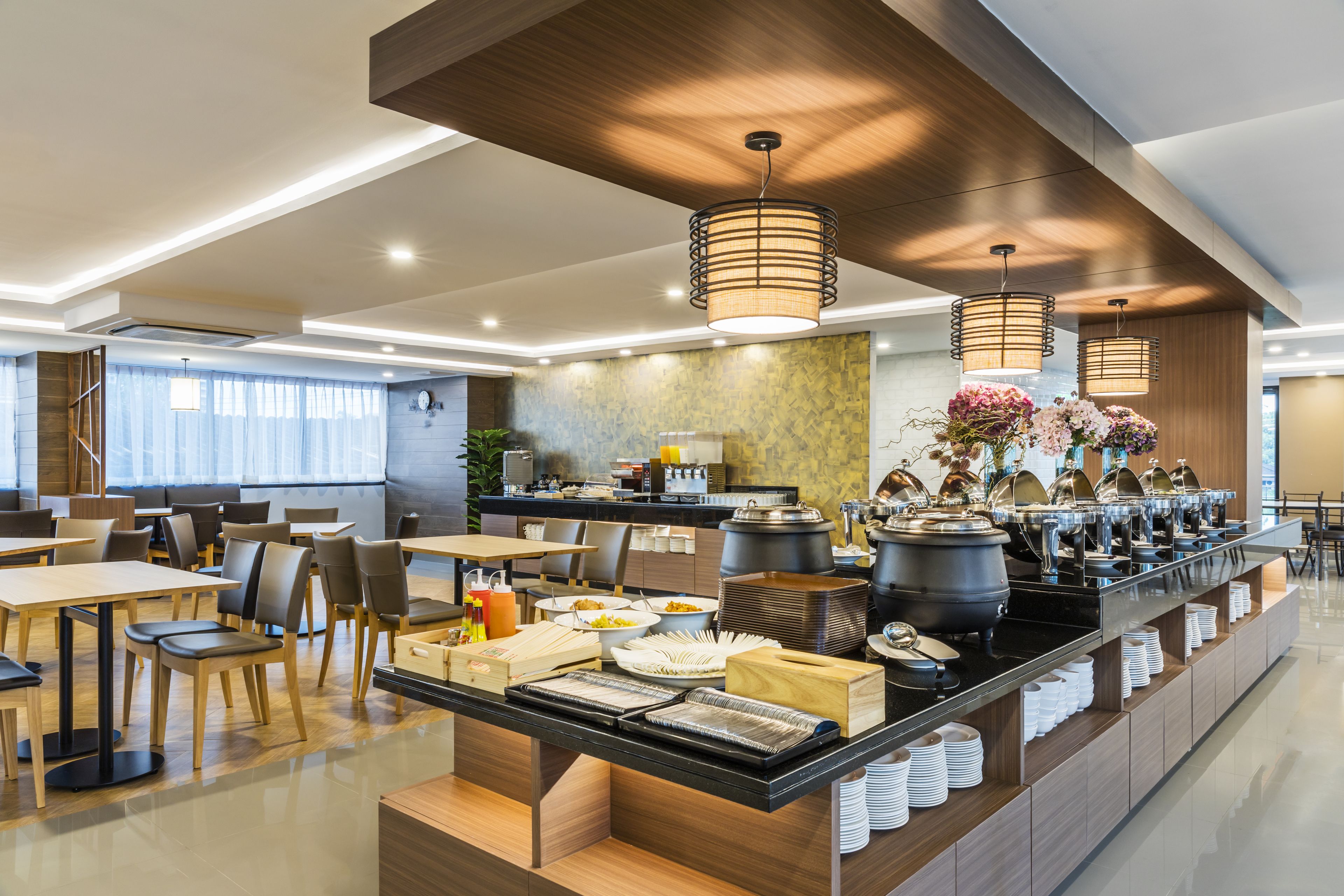 Un espace de restauration moderne dans un hôtel, avec un service de buffet, des tables disposées de manière agréable et un éclairage contemporain.