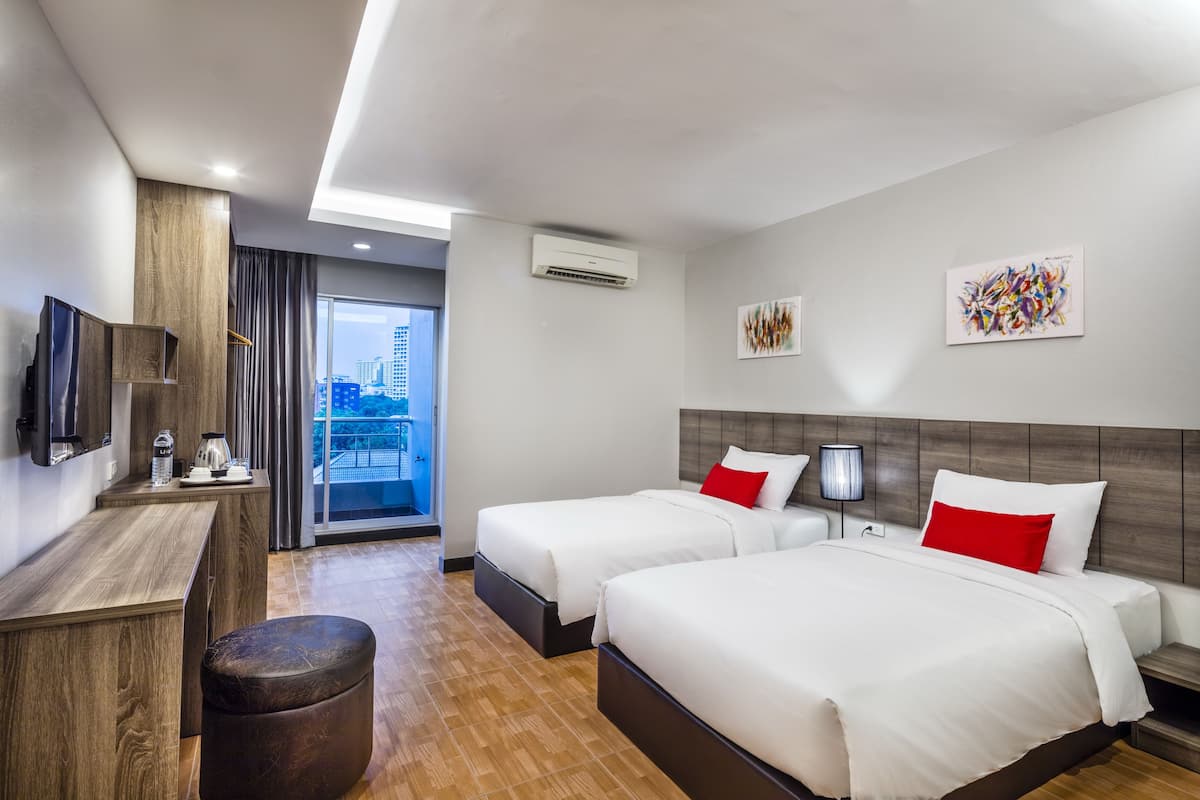 A hotel room with two beds, a desk, a TV, an air conditioner, and a window with a city view.