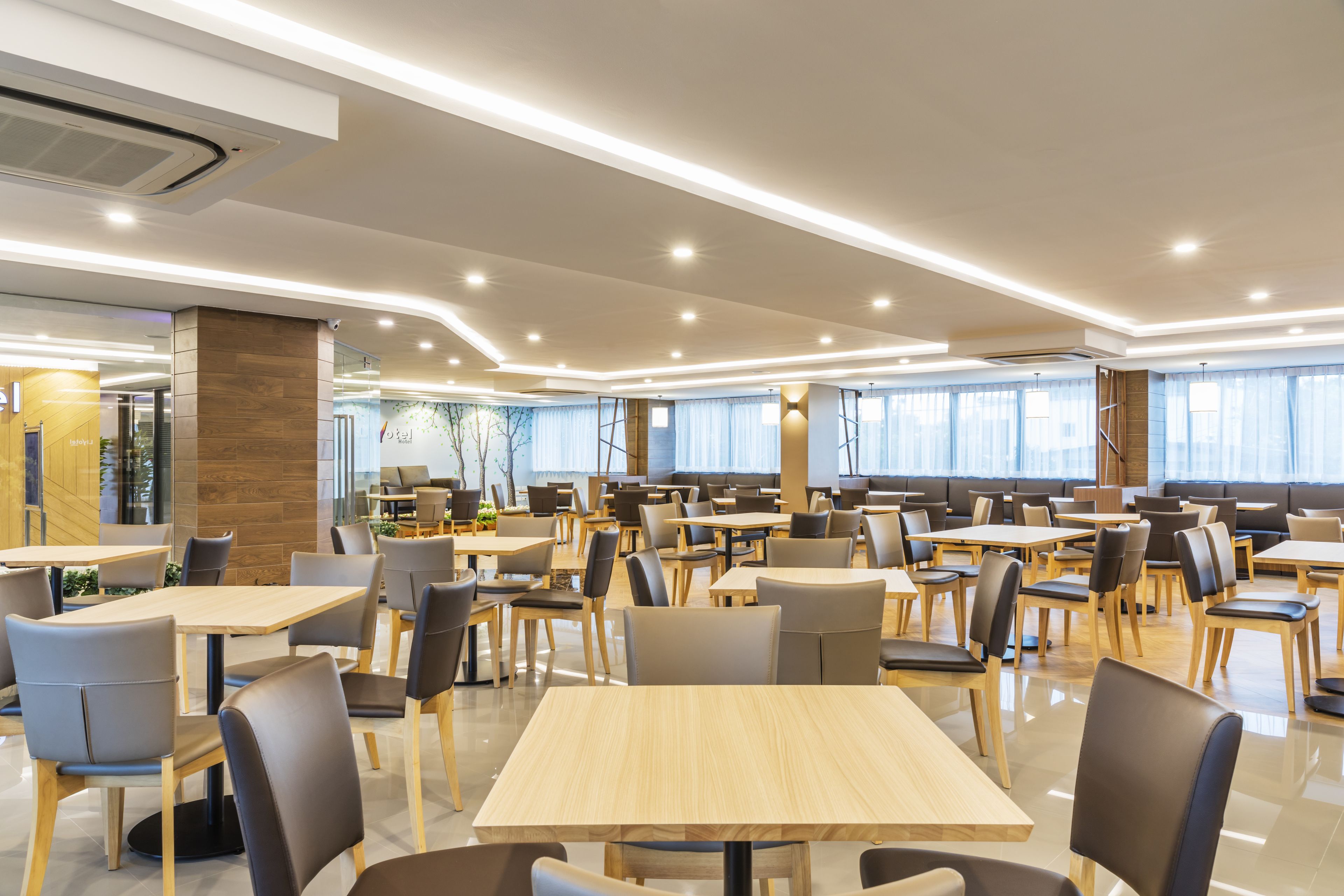 Un amplio comedor interior con varias mesas y sillas, ventanas grandes y un diseño moderno en el techo.