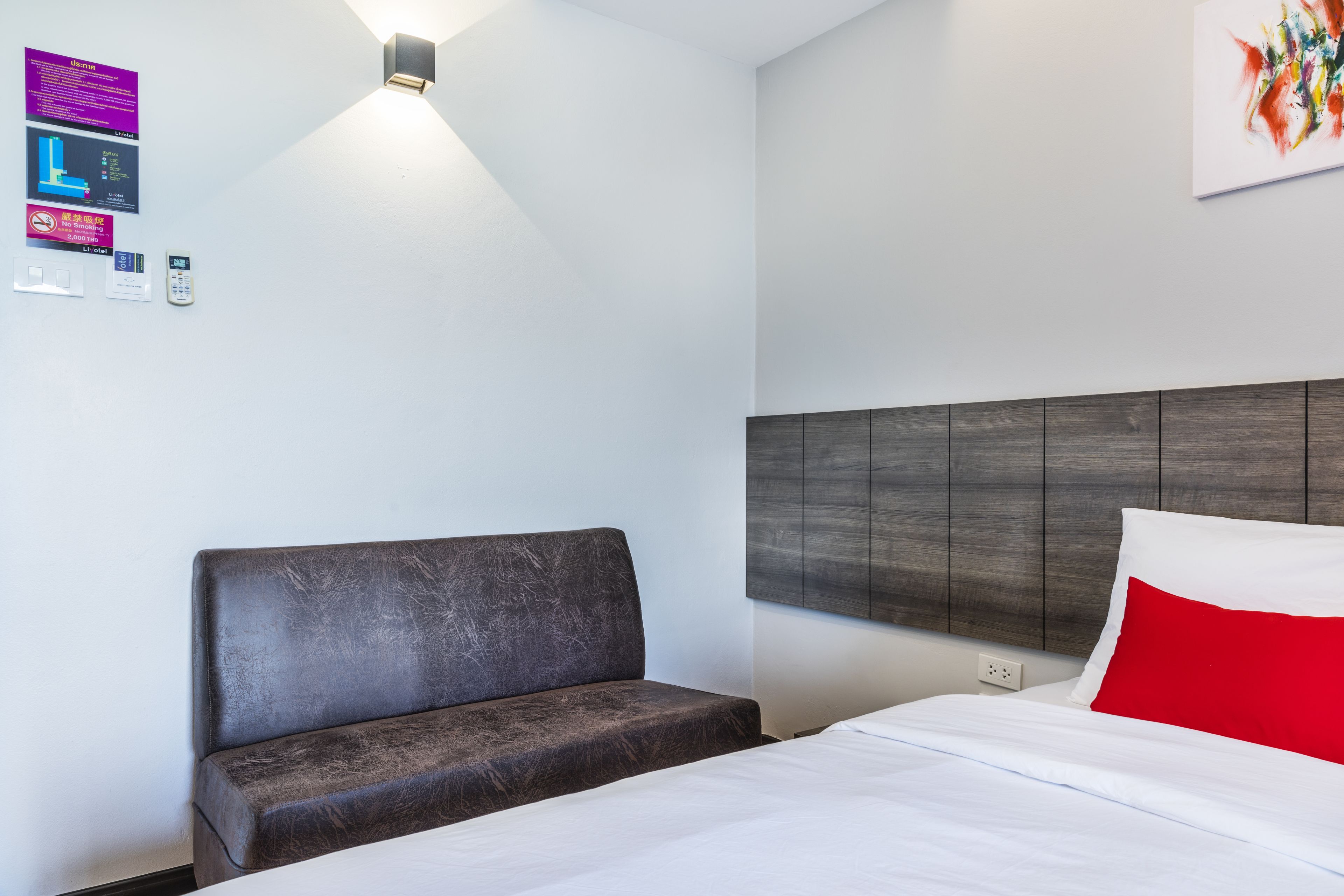 A modern hotel room with a bed, a sofa, a wall-mounted light, and a painting.