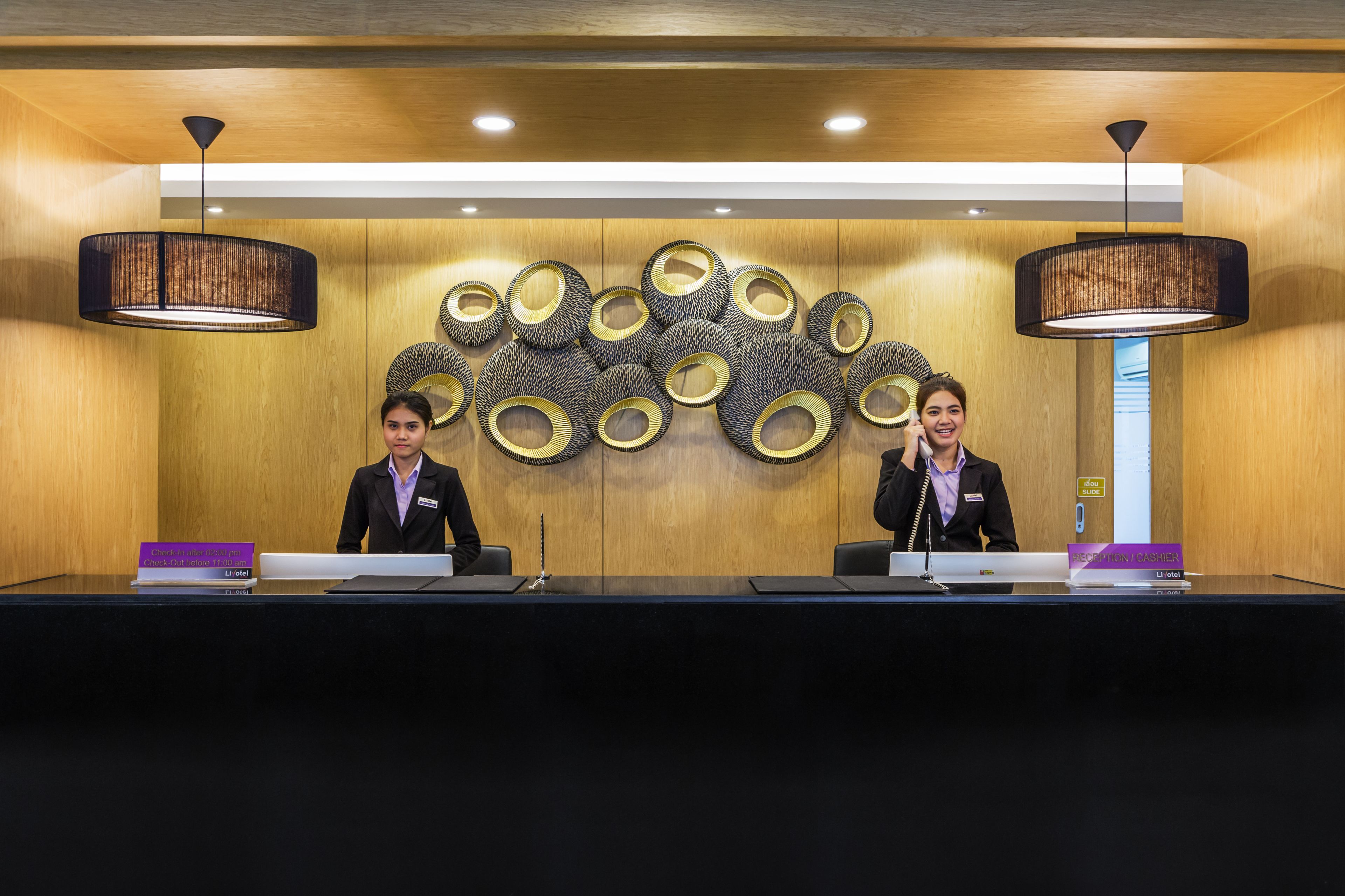 A reception desk with two staff members, a wooden wall with circular decorations, and pendant lighting.
