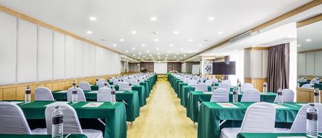 A conference room with rows of tables, each covered with a green tablecloth and white chairs.