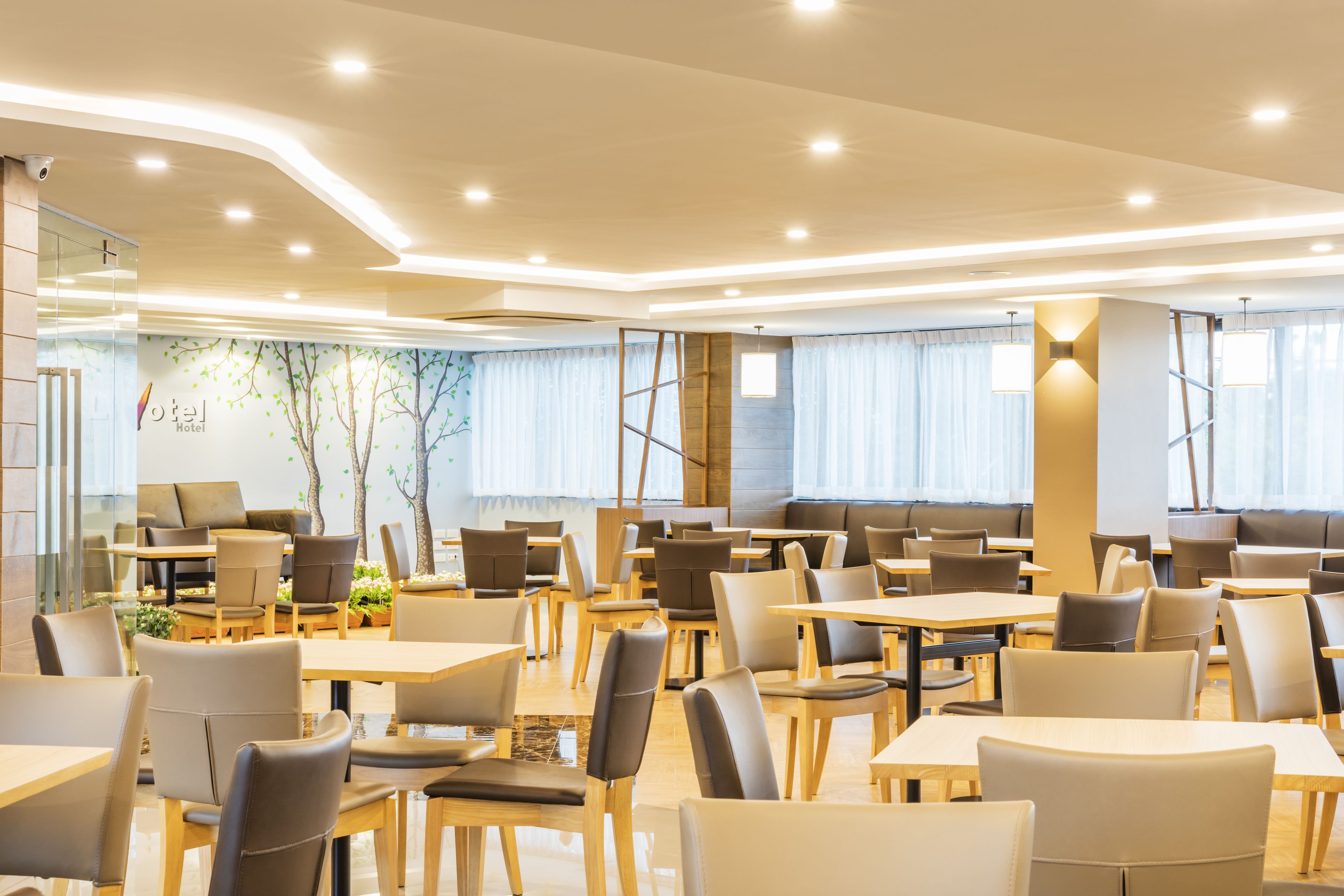 En modern hotellobby med flera sittgrupper, inklusive bord och stolar, och ett stort fönster med gardiner.