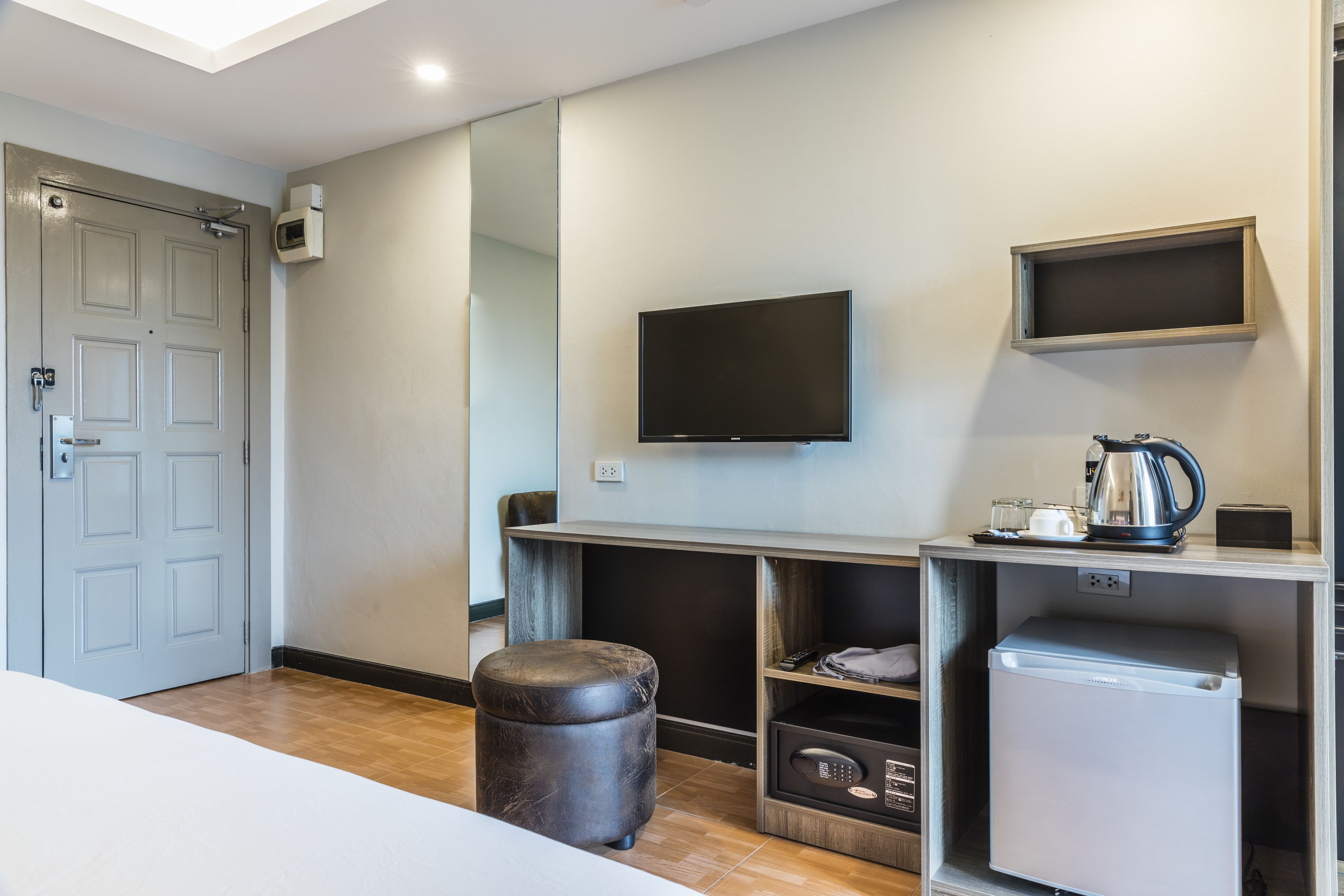 Une chambre moderne dotée d’un téléviseur à écran plat fixé au mur, d’une petite kitchenette équipée d’une machine à café et d’un réfrigérateur compact.