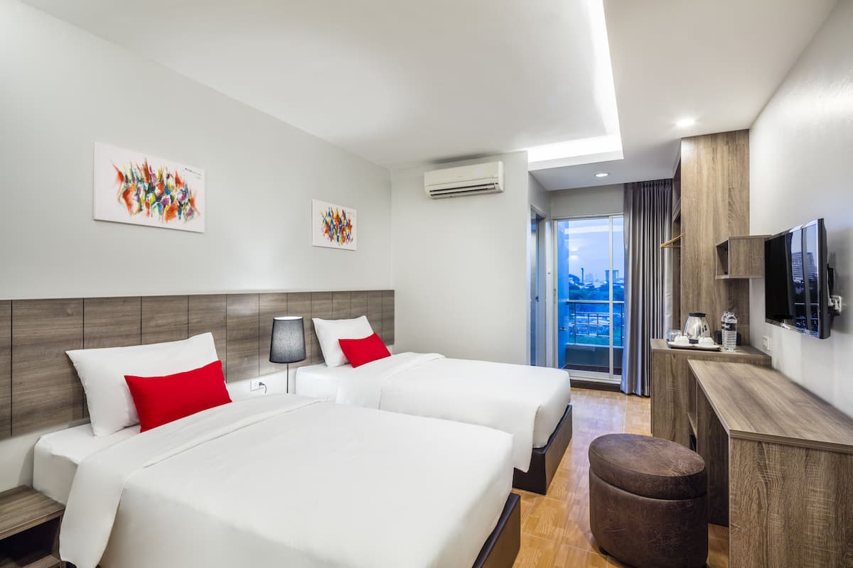 A modern hotel room with two beds, a desk, a TV, and a city view.