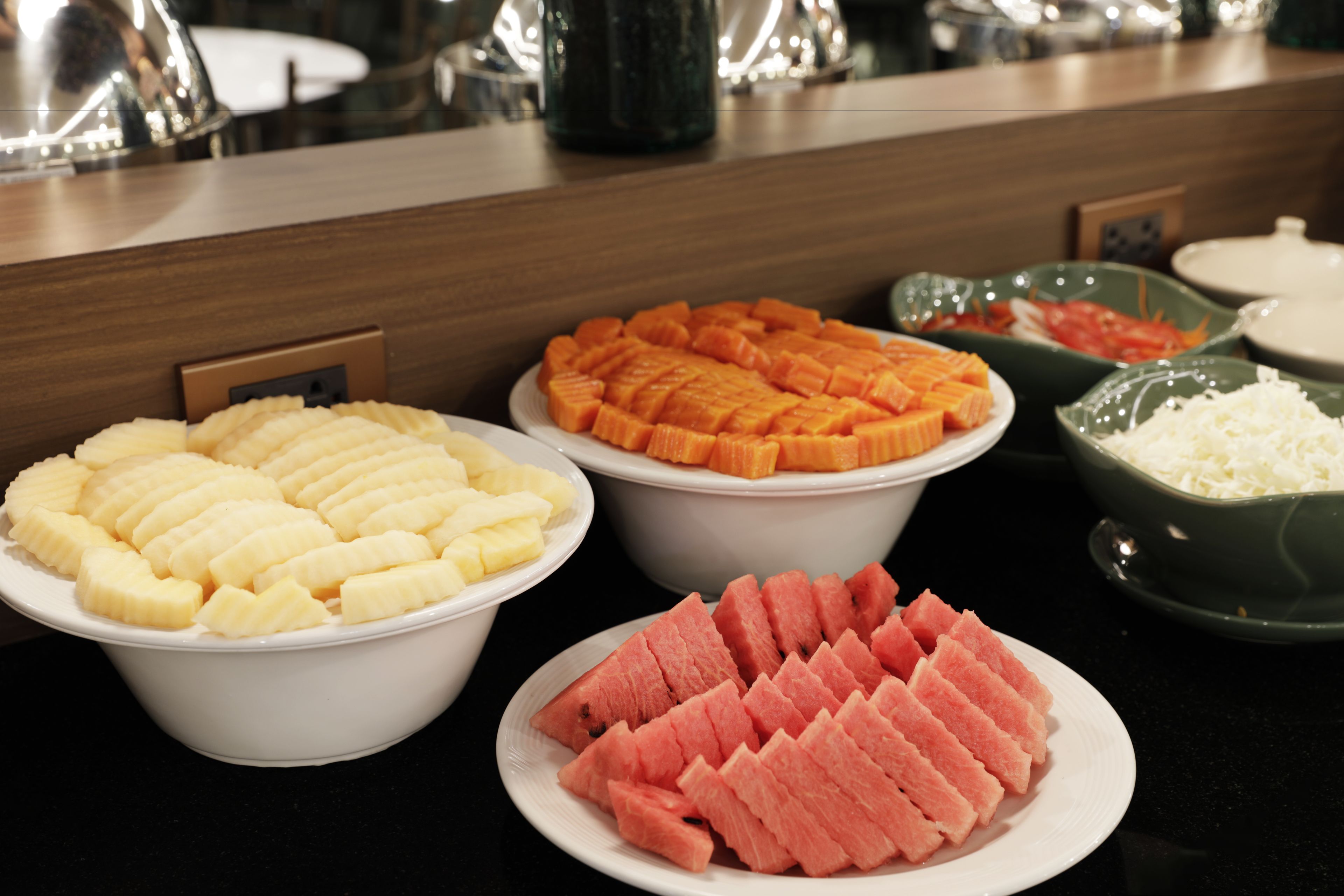 Una mesa de buffet con diversos alimentos, entre ellos frutas y verduras cortadas.