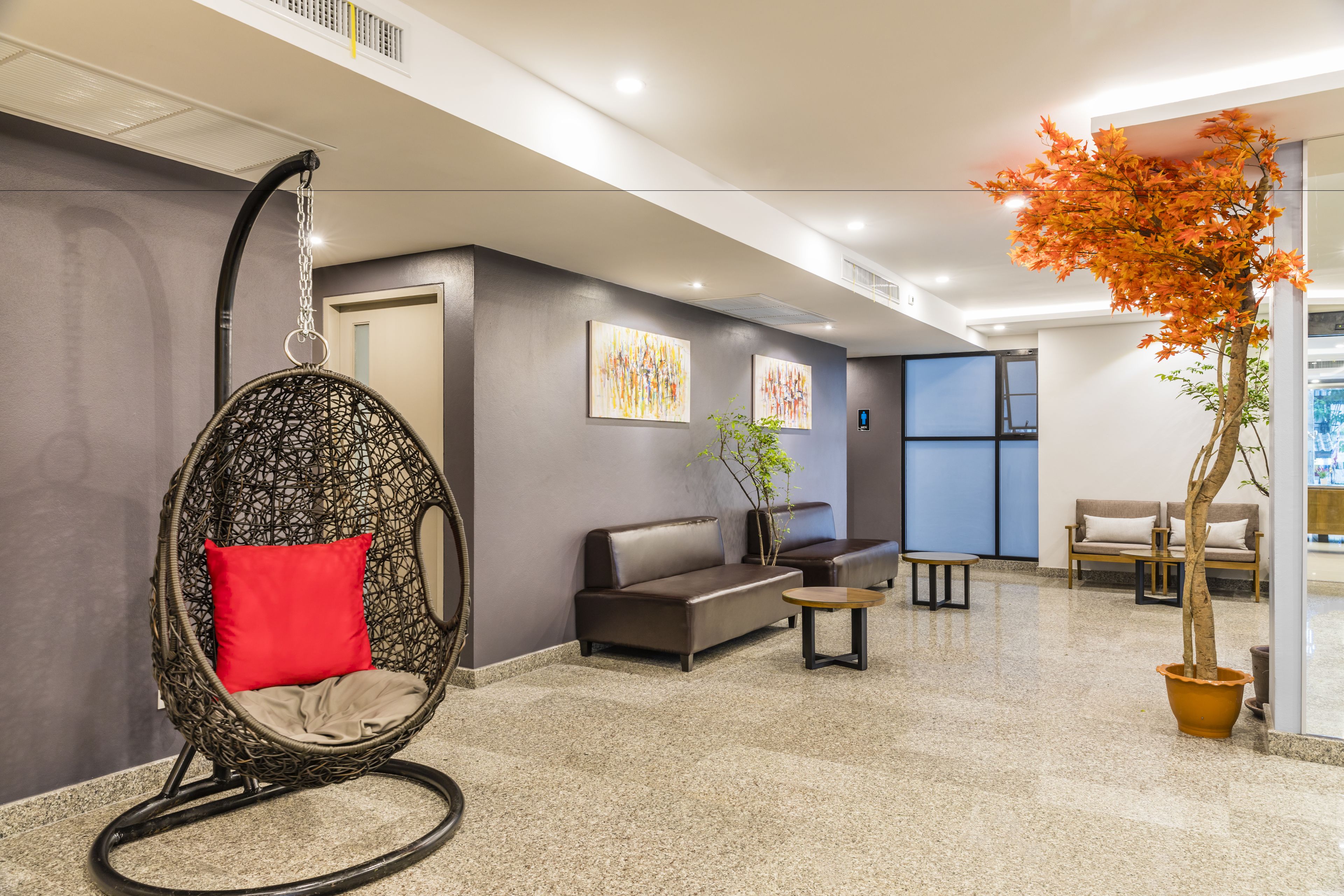 Un hall d’entrée moderne avec un fauteuil en rotin, des canapés, une table basse et un arbre en pot.