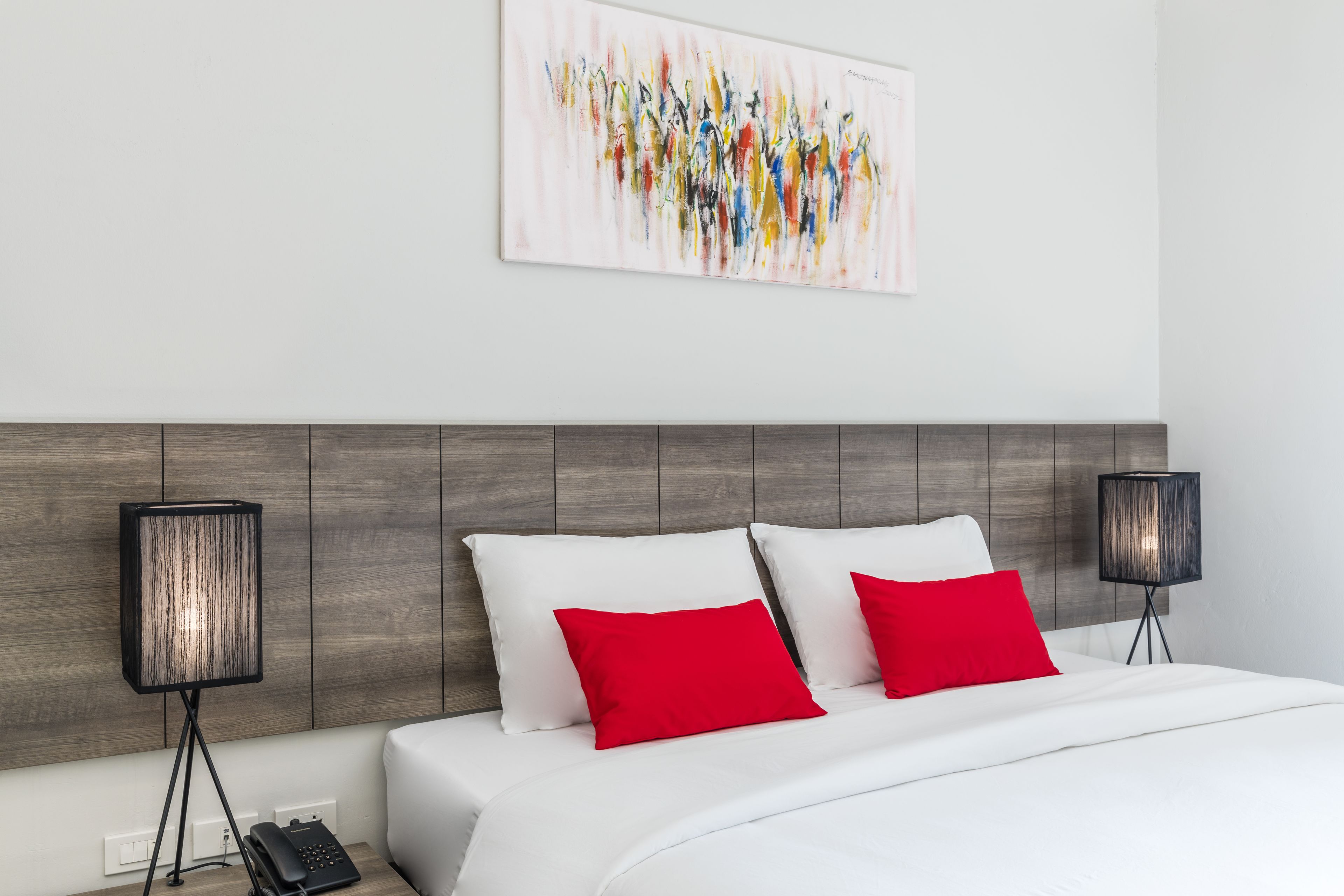 A modern hotel room with a wooden headboard, white bedding, and two red pillows.