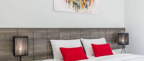 A modern hotel room with a wooden headboard, white bedding, and two red pillows.