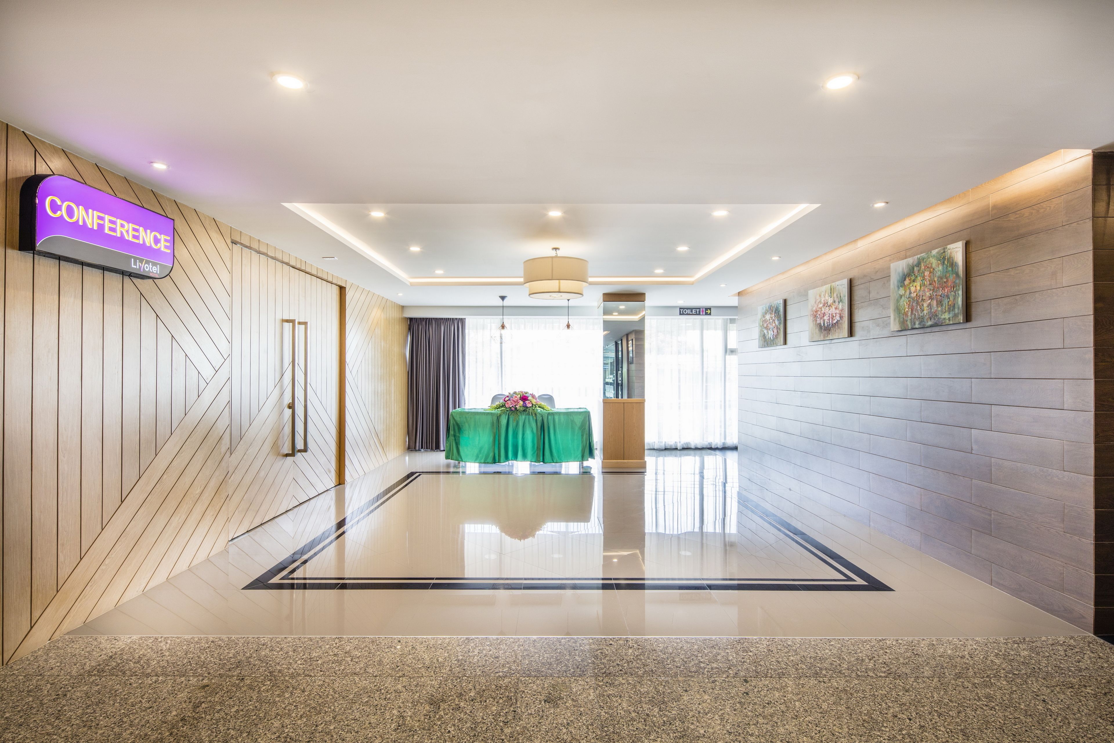 A modern hotel lobby with a conference area, a reception desk, and a restroom sign.