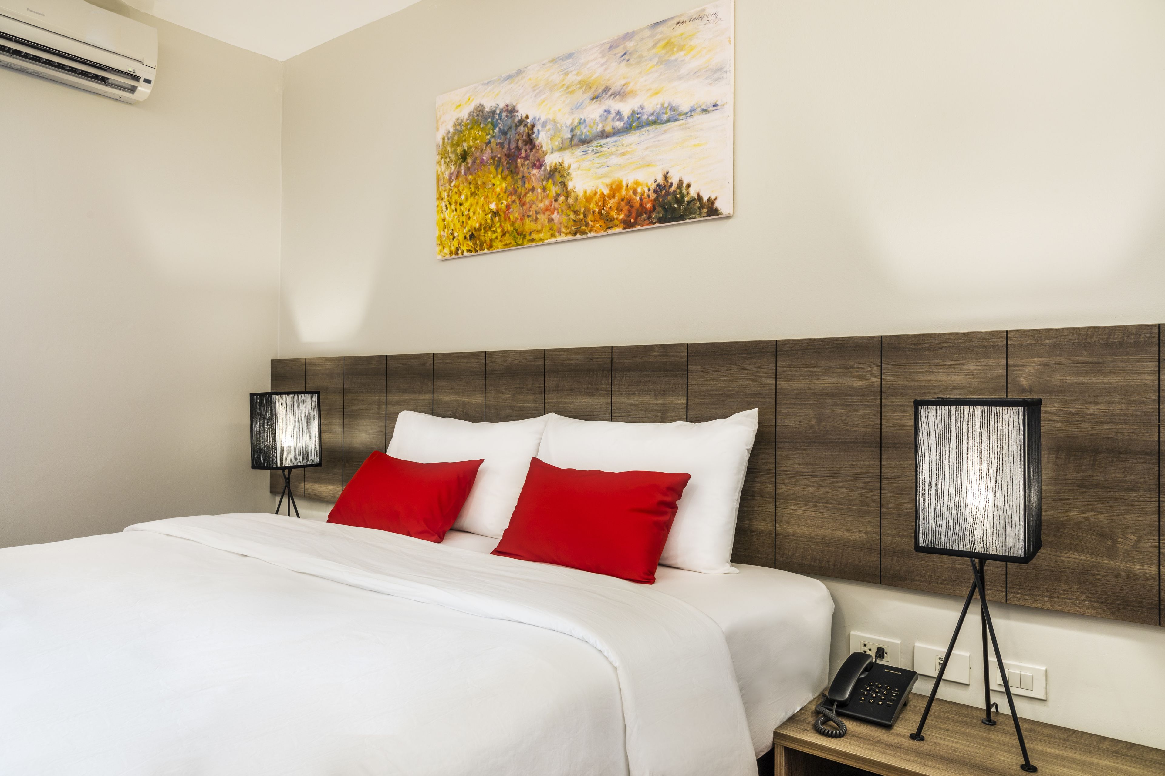 Una habitación de hotel con una cama grande, dos lámparas de noche, un cuadro en la pared y un teléfono en la mesita.