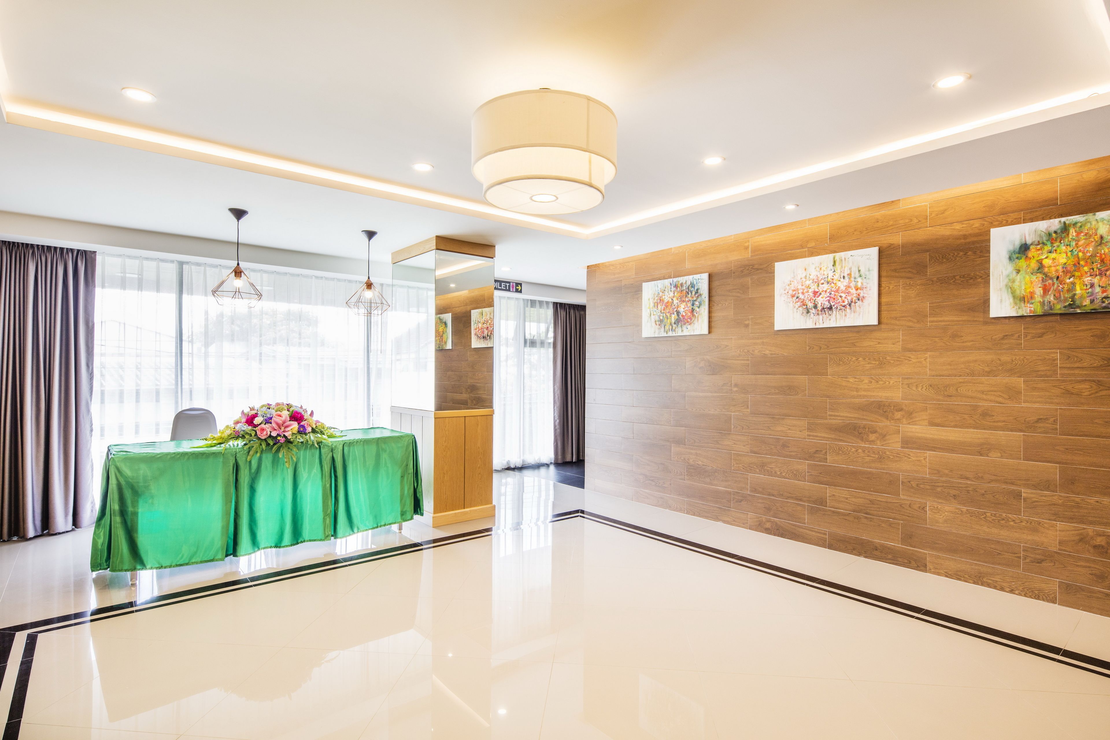 A modern hotel lobby with a green table, floral centerpiece, wooden wall panels, and artwork.