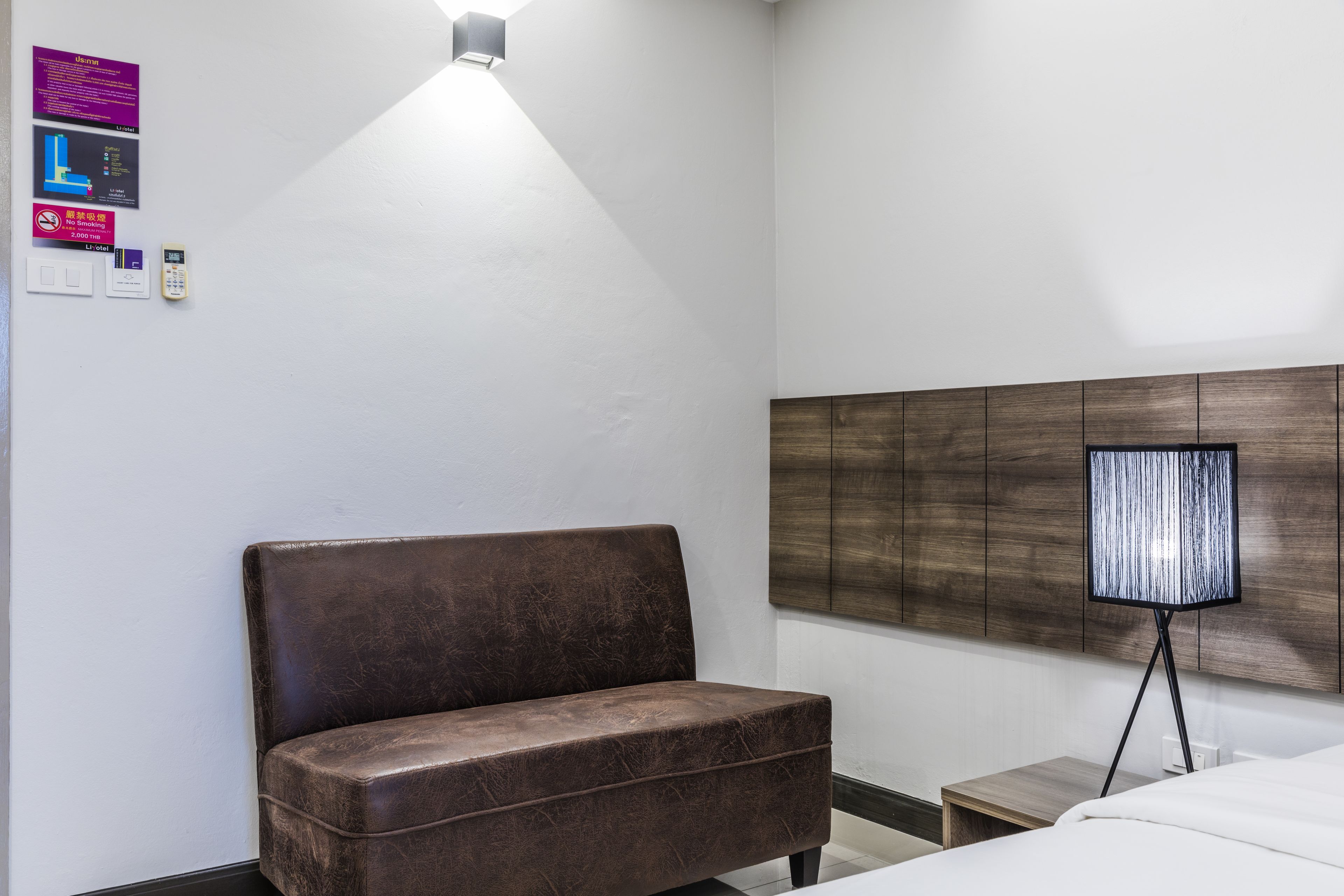 Una habitación de hotel con un sofá de cuero marrón, una mesita de noche, una lámpara y una cama.