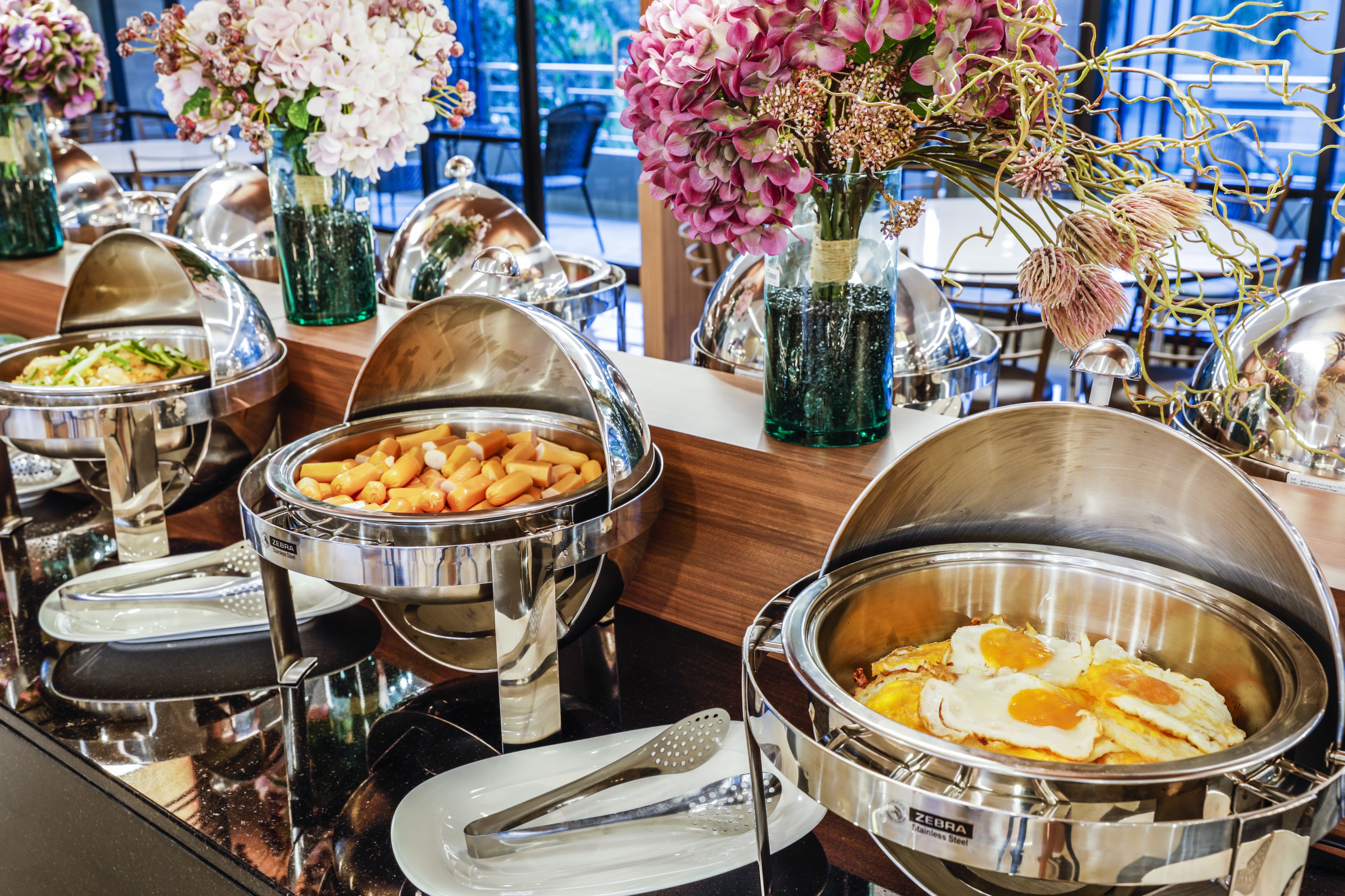 A buffet setup with various food items and decorative flowers.