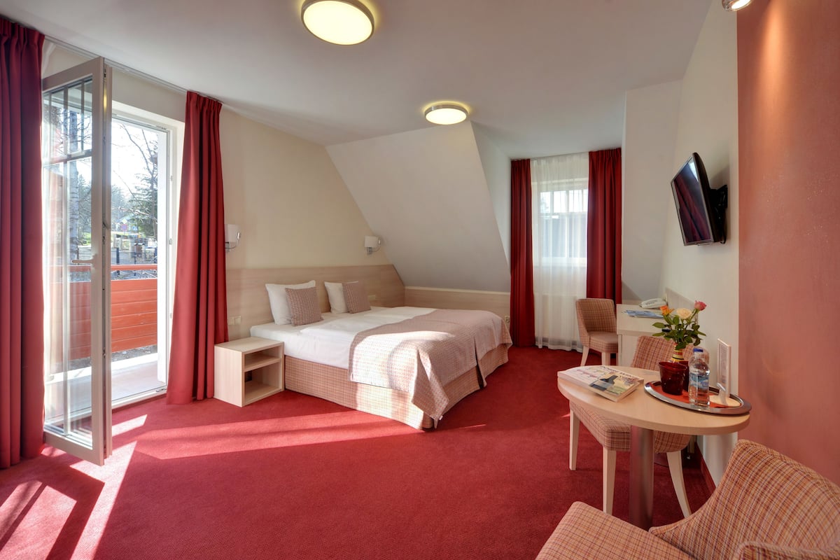A hotel room with a bed, a desk with a chair, a TV, and a window with curtains.