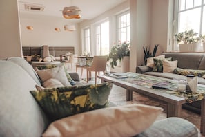 A spacious living room with a large sofa, a coffee table with a board game, and a dining area with chairs and a table.