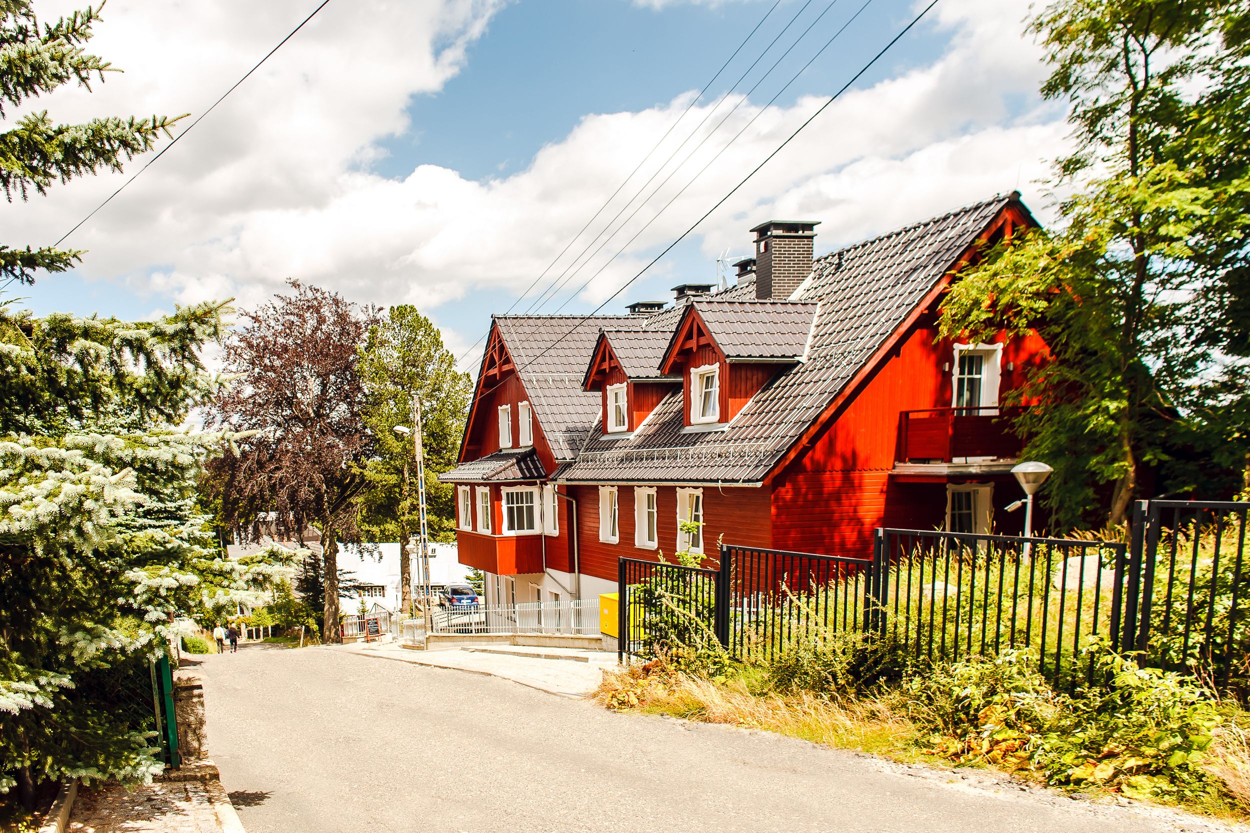 Ein rotes Haus mit einem geneigten Dach, einer weißen Tür und einem schwarzen Zaun davor.