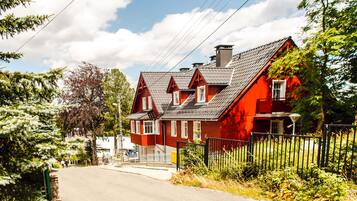 Ein rotes Haus mit einem geneigten Dach, einer weißen Tür und einem schwarzen Zaun davor.