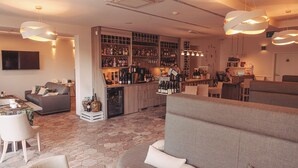 Uma área de bar moderna com diversas garrafas de bebidas, uma máquina de café e um espaço de estar com sofás e uma mesa.