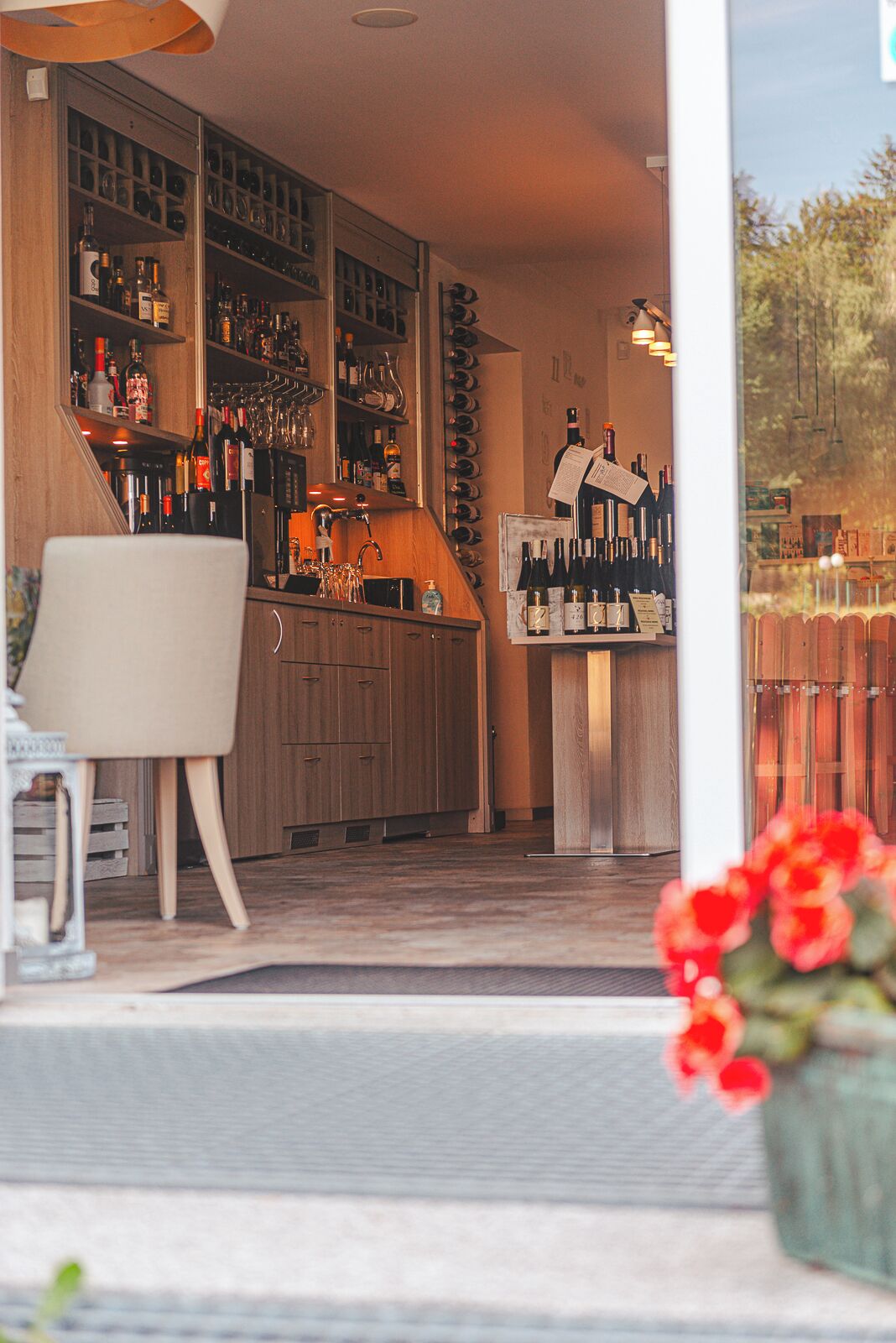 A bar area with shelves of bottles and glasses, a counter with a menu, and a chair.