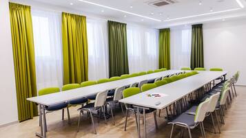 Ein Konferenzraum mit einem langen Tisch, mehreren Stühlen und großen Fenstern mit grünen Vorhängen.