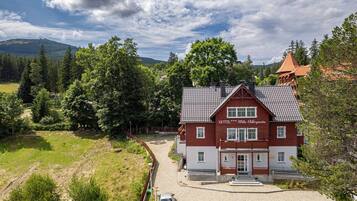 A red and white hotel with a tiled roof, surrounded by lush greenery and mountains.