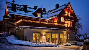 Uma grande casa de madeira com vários andares, telhados cobertos de neve e uma entrada bem iluminada.