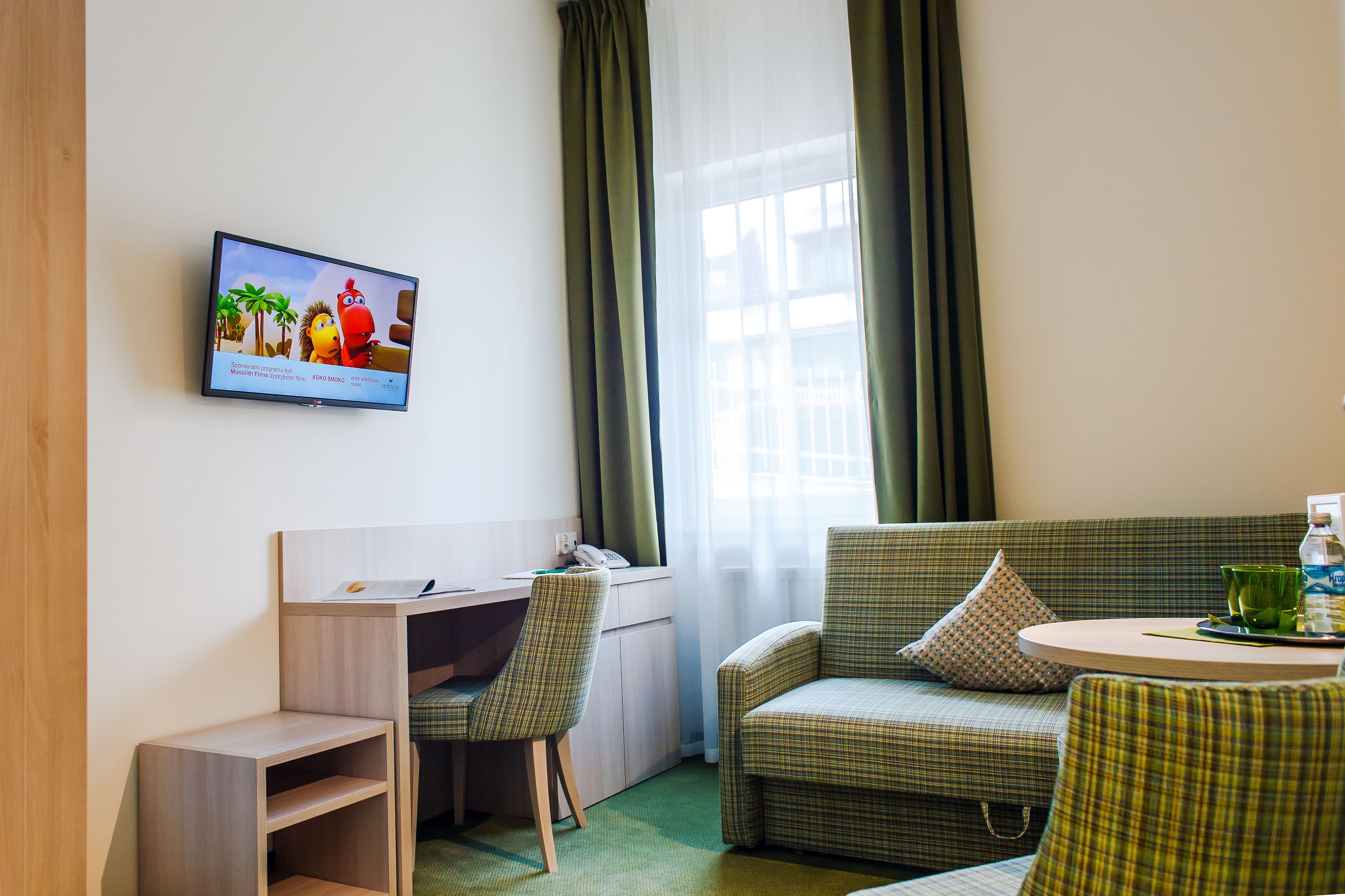 A hotel room with a desk, a chair, a sofa, a television, and a window with curtains.