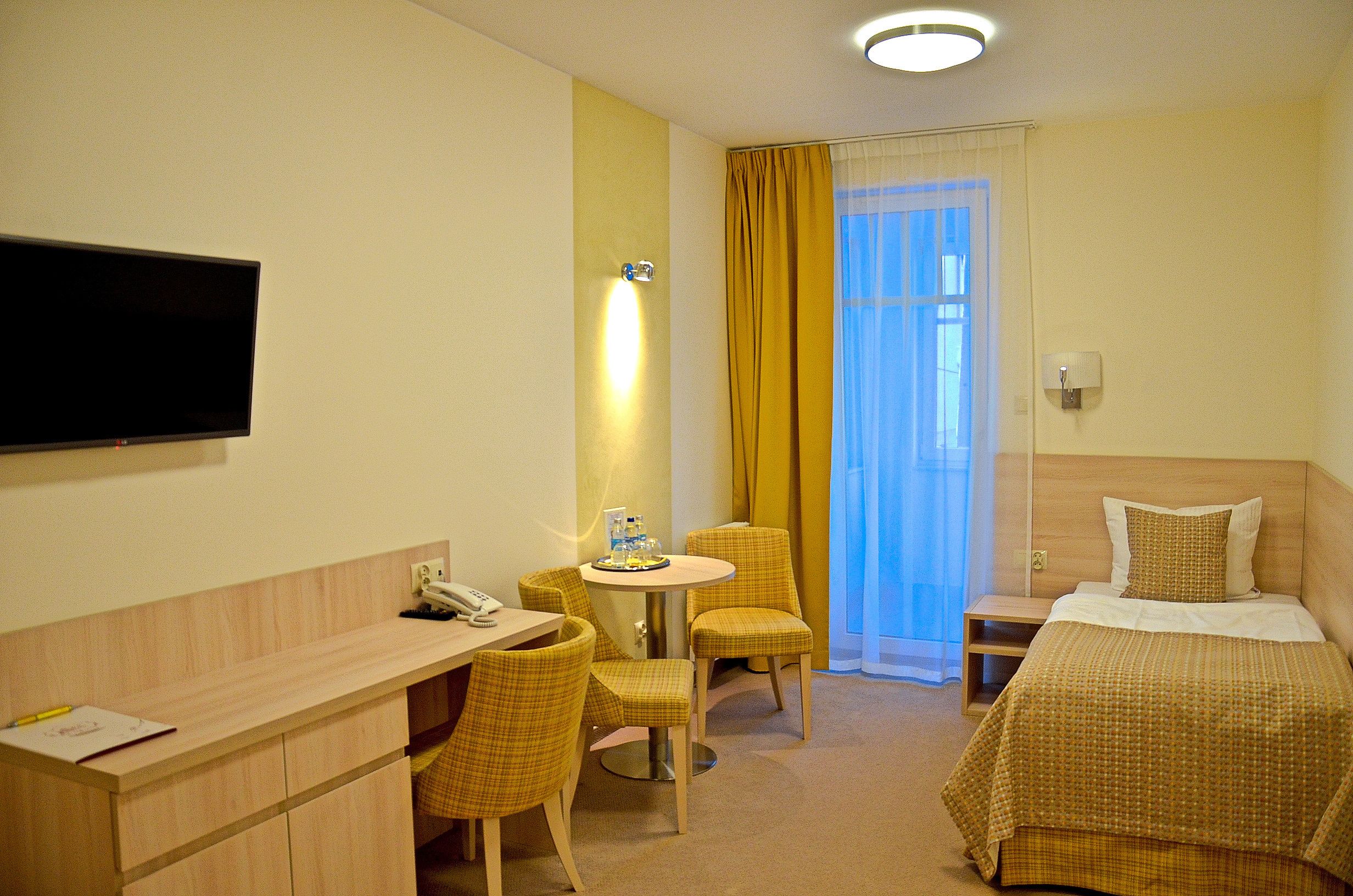 Una habitación de hotel con cama, escritorio, silla, televisor y ventana con cortinas.