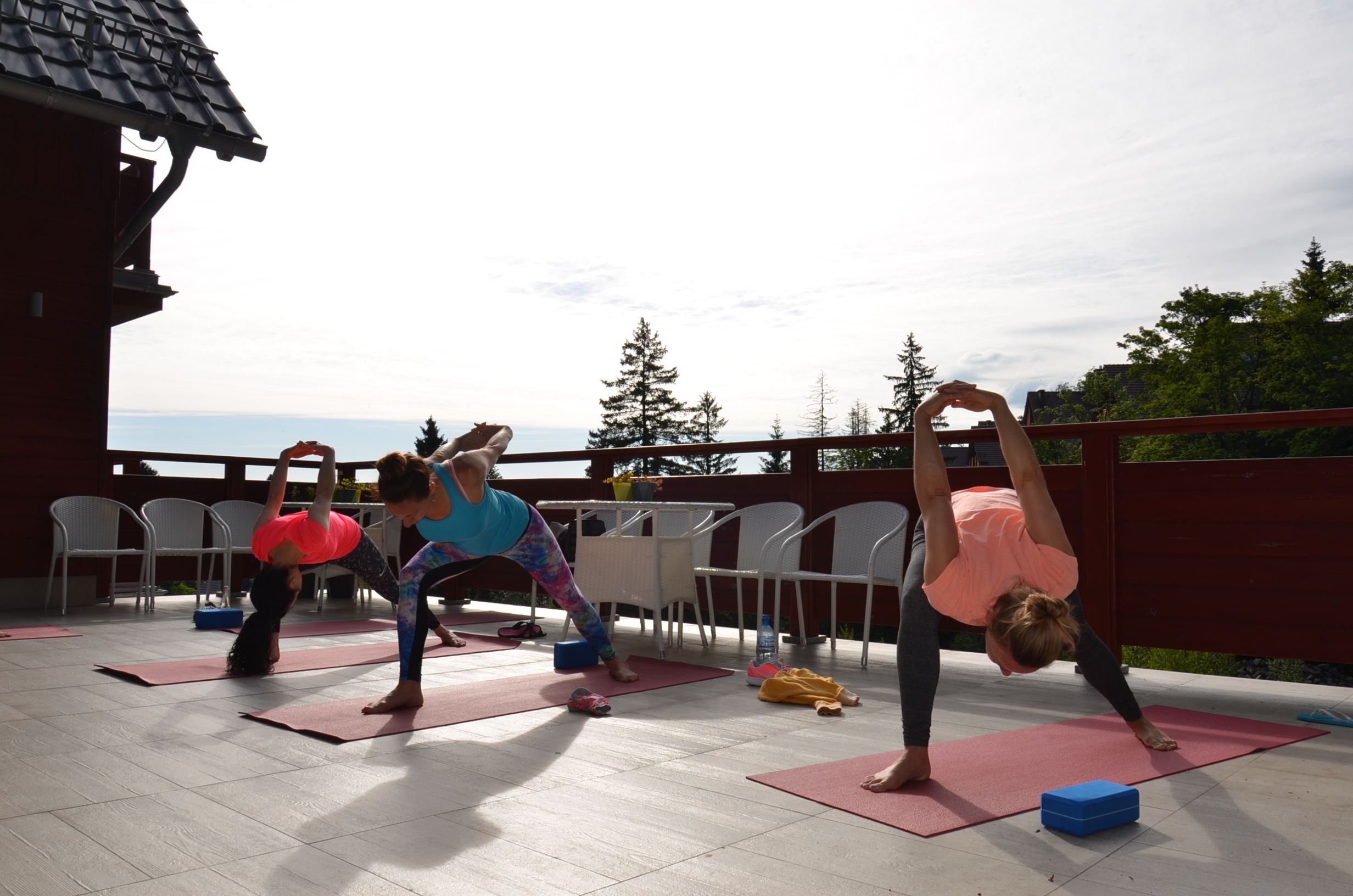 A group of people performing yoga on outdoor mats in an open area with chairs and tables.
