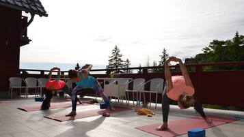 A group of people performing yoga on outdoor mats in an open area with chairs and tables.