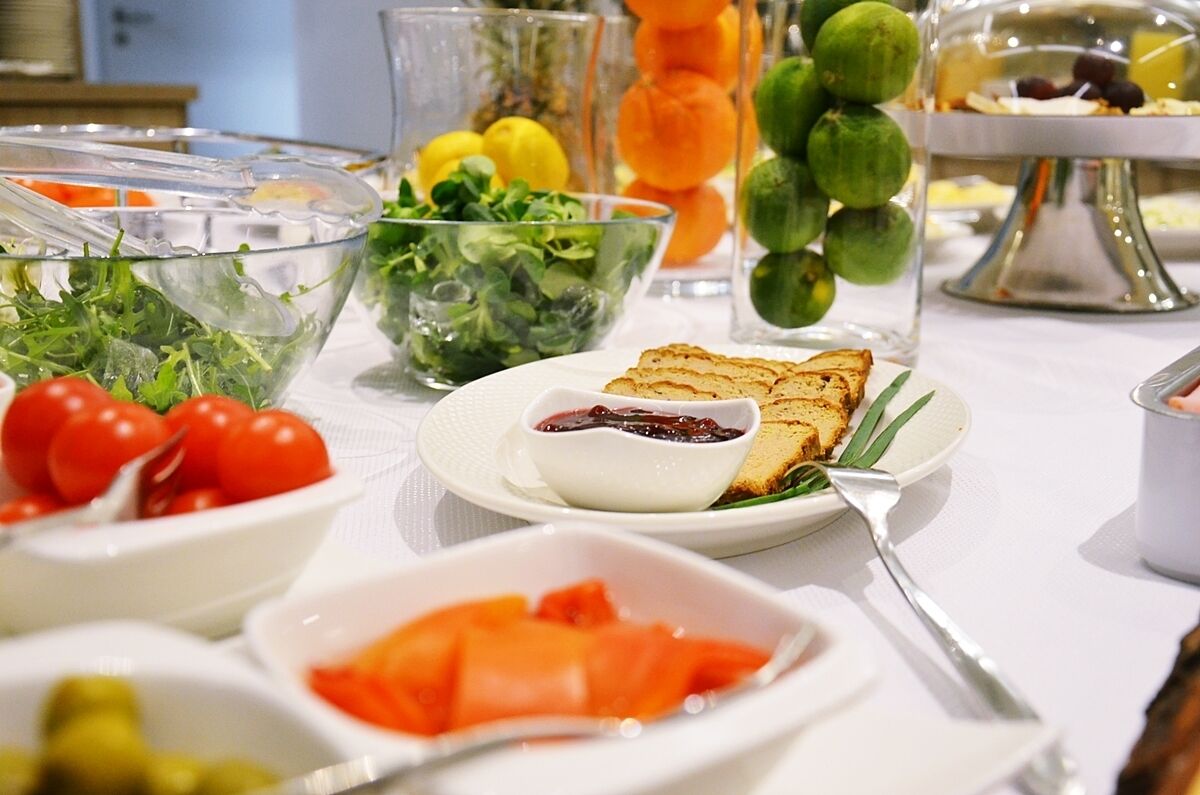 Una mesa de buffet con diversos alimentos, entre ellos ensaladas, tomates y un plato con tostadas y mermelada.