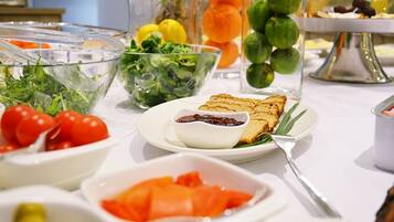 Una mesa de buffet con diversos alimentos, entre ellos ensaladas, tomates y un plato con tostadas y mermelada.