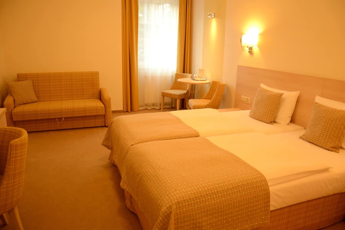 A hotel room with two beds, a sofa, and a small table.