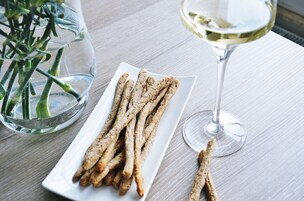 Un plato de aperitivos crujientes y una copa de vino blanco sobre una mesa de madera.